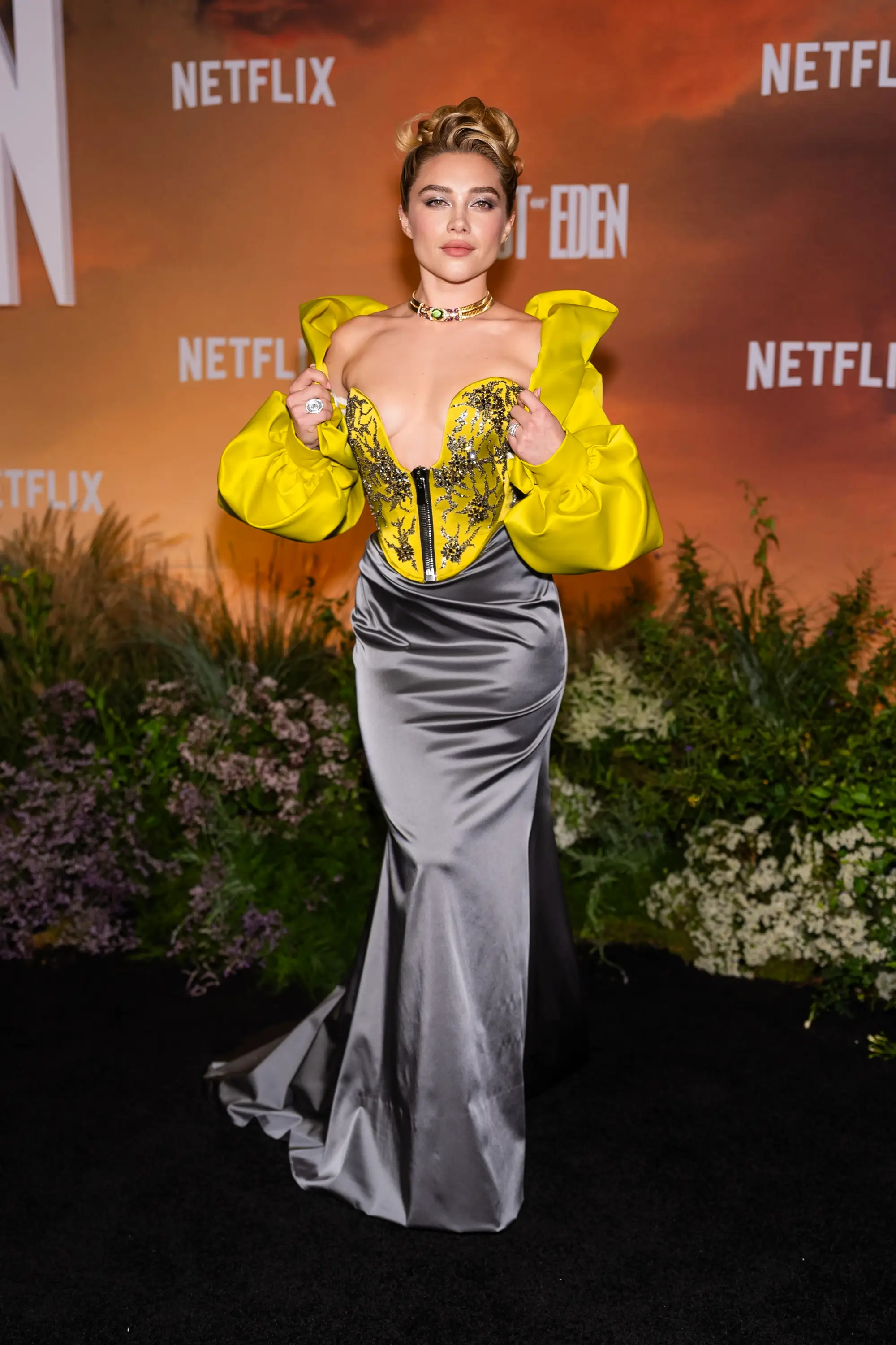 Florence Pugh poses on a Netflix event carpet in a yellow corset top and silver skirt.