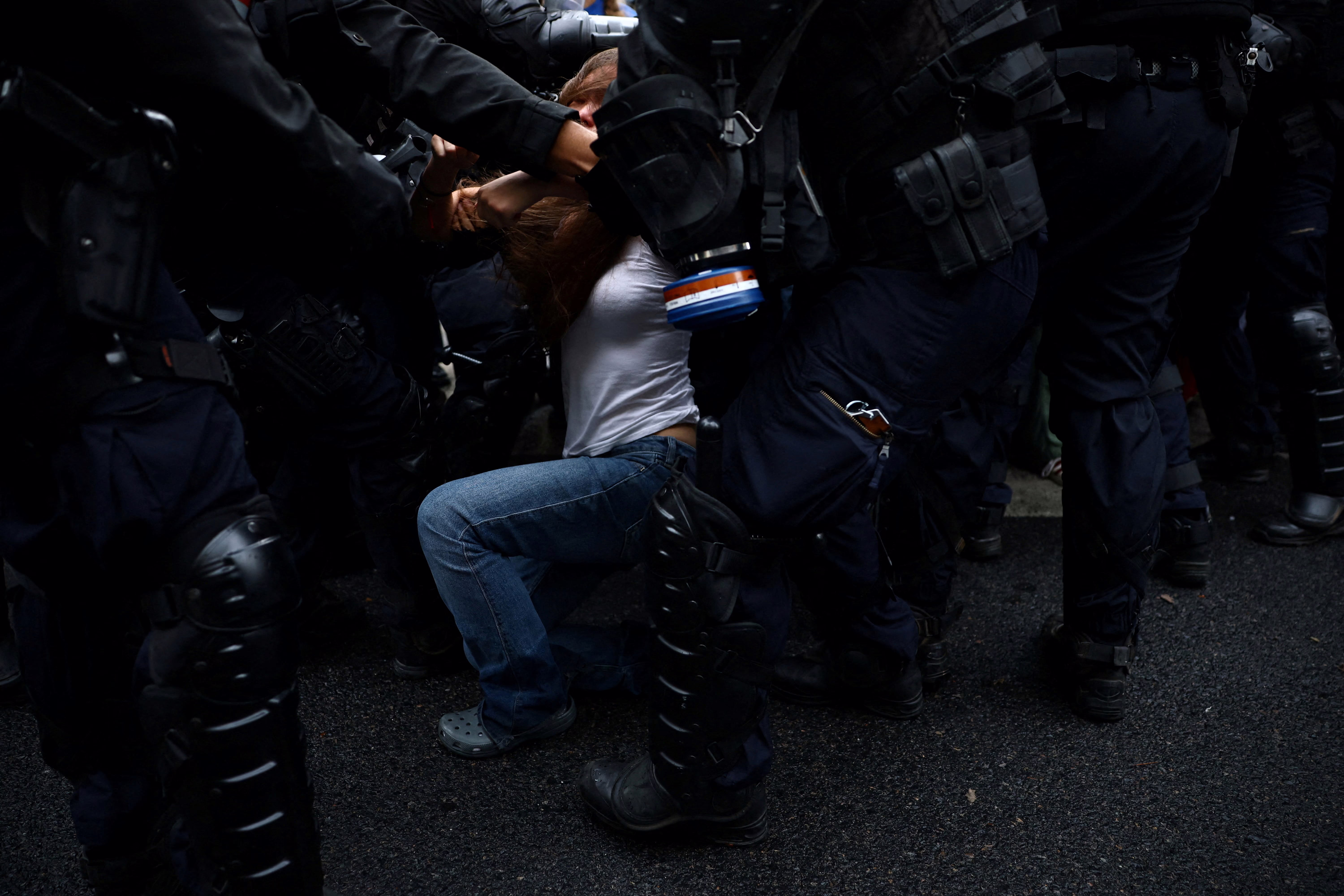 A student protester falls as they are detained by many riot police officers surrounding them.