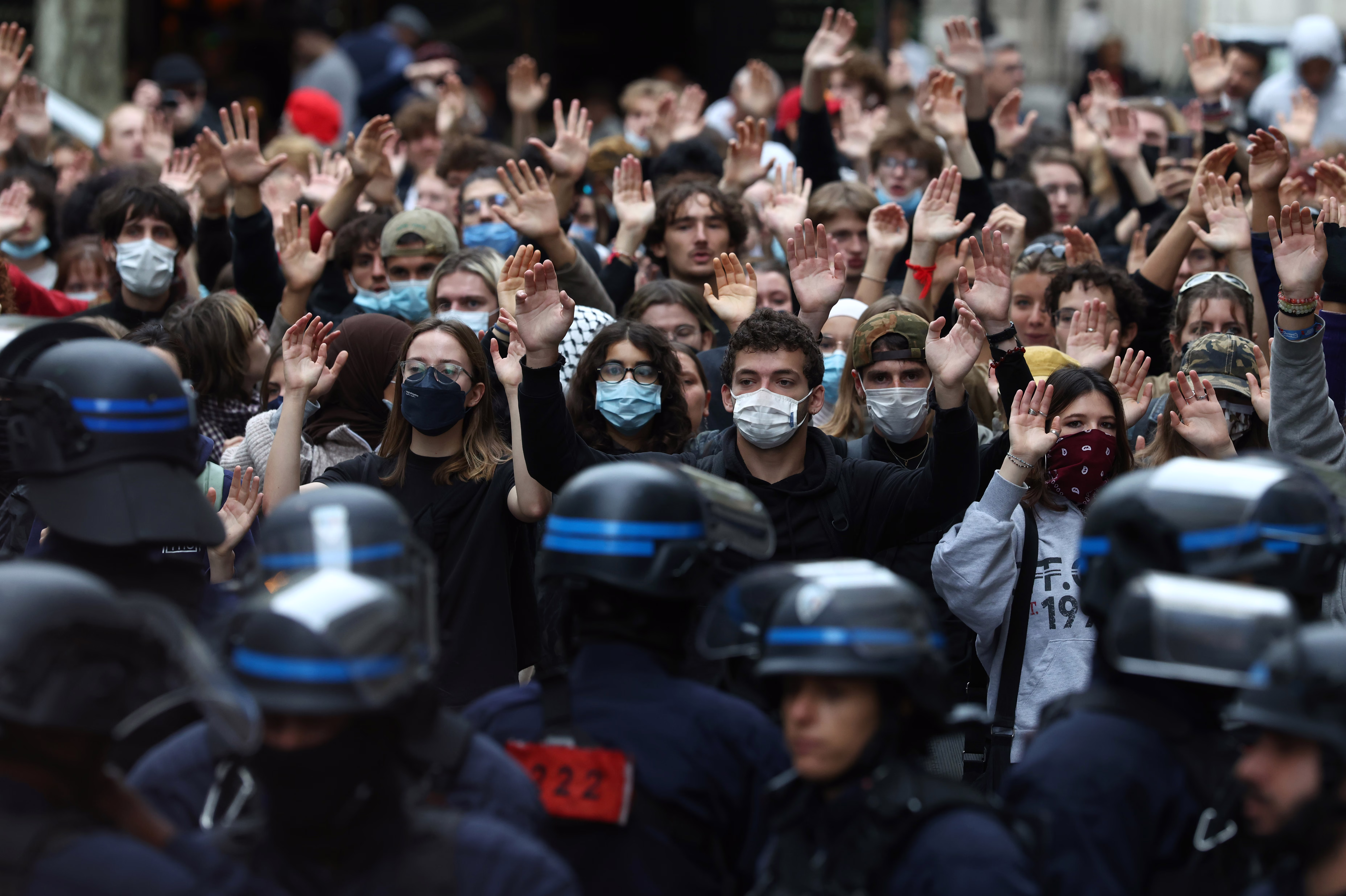 Protesting students raise their hands in front of riot police officers. 