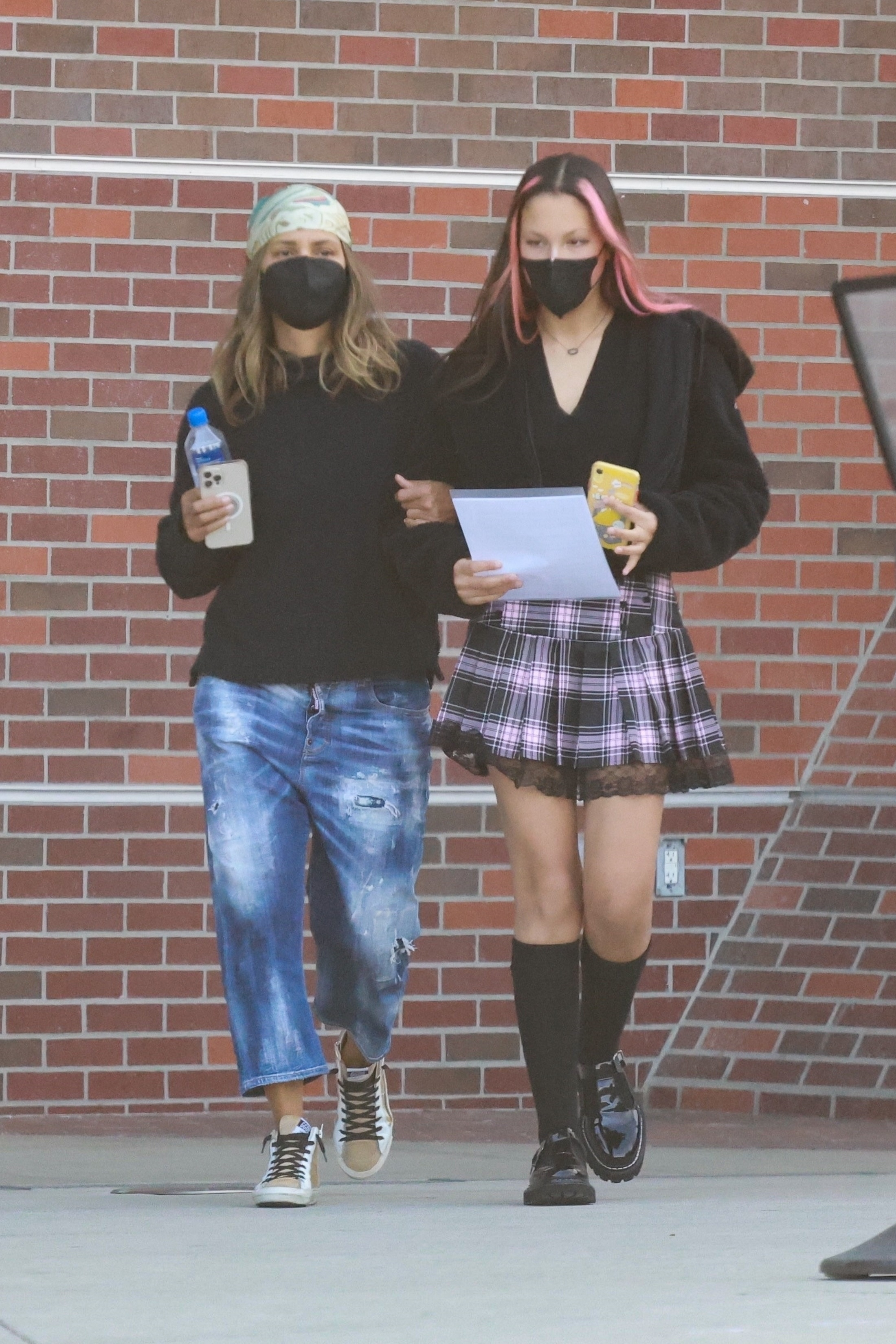 Halle Berry and her daughter Nahla Aubry walking outdoors in front of a brick wall, both wearing black face masks.