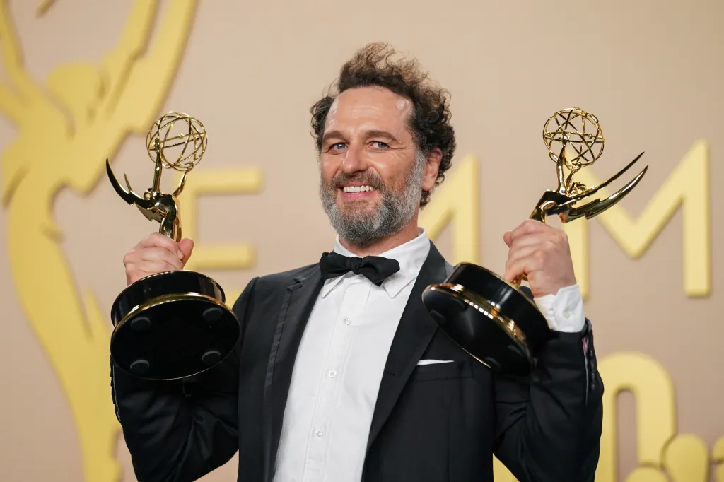 Matthew Rhys poses in the press room holding two Emmy awards.