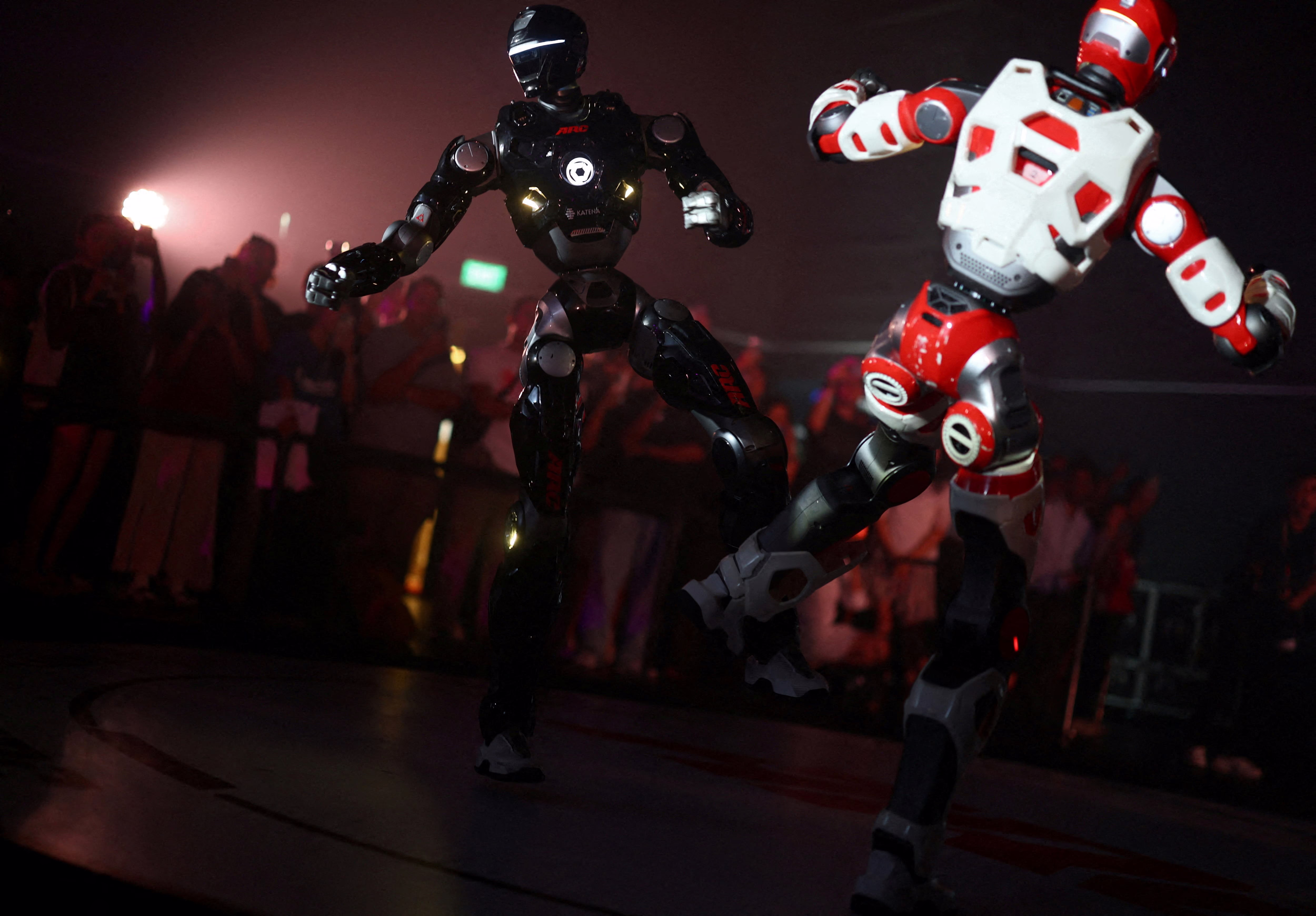 People watch as two humanoid robots fight.