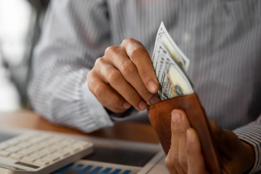 Close-up of a person putting American dollar bills into a leather wallet.