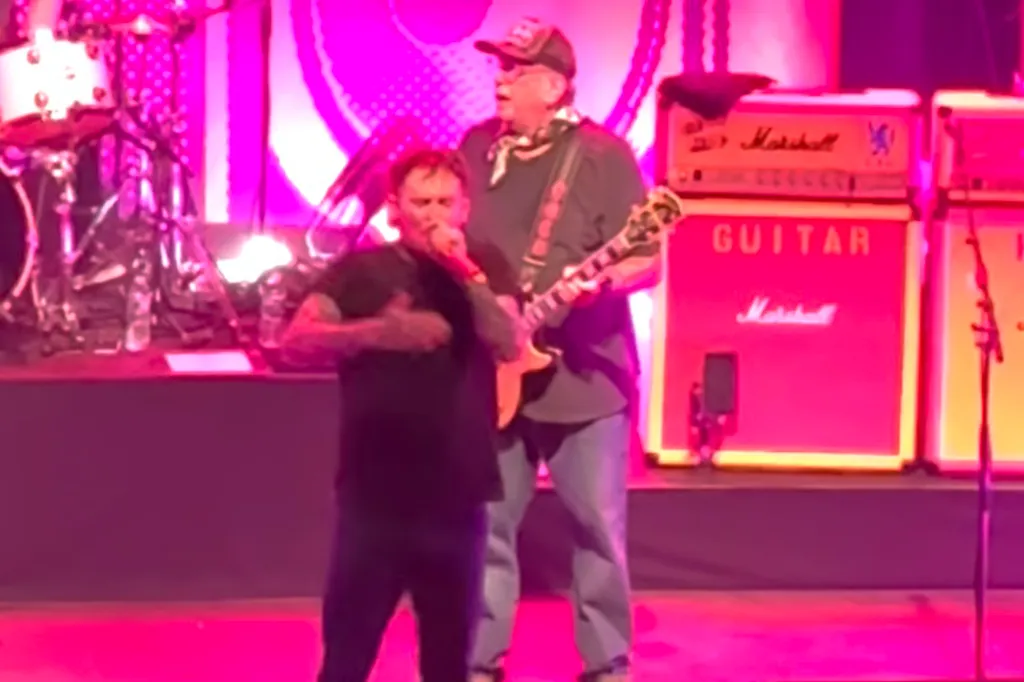 Sex Pistols frontman Frank Carter on stage with a guitarist against a vibrant pink backdrop.