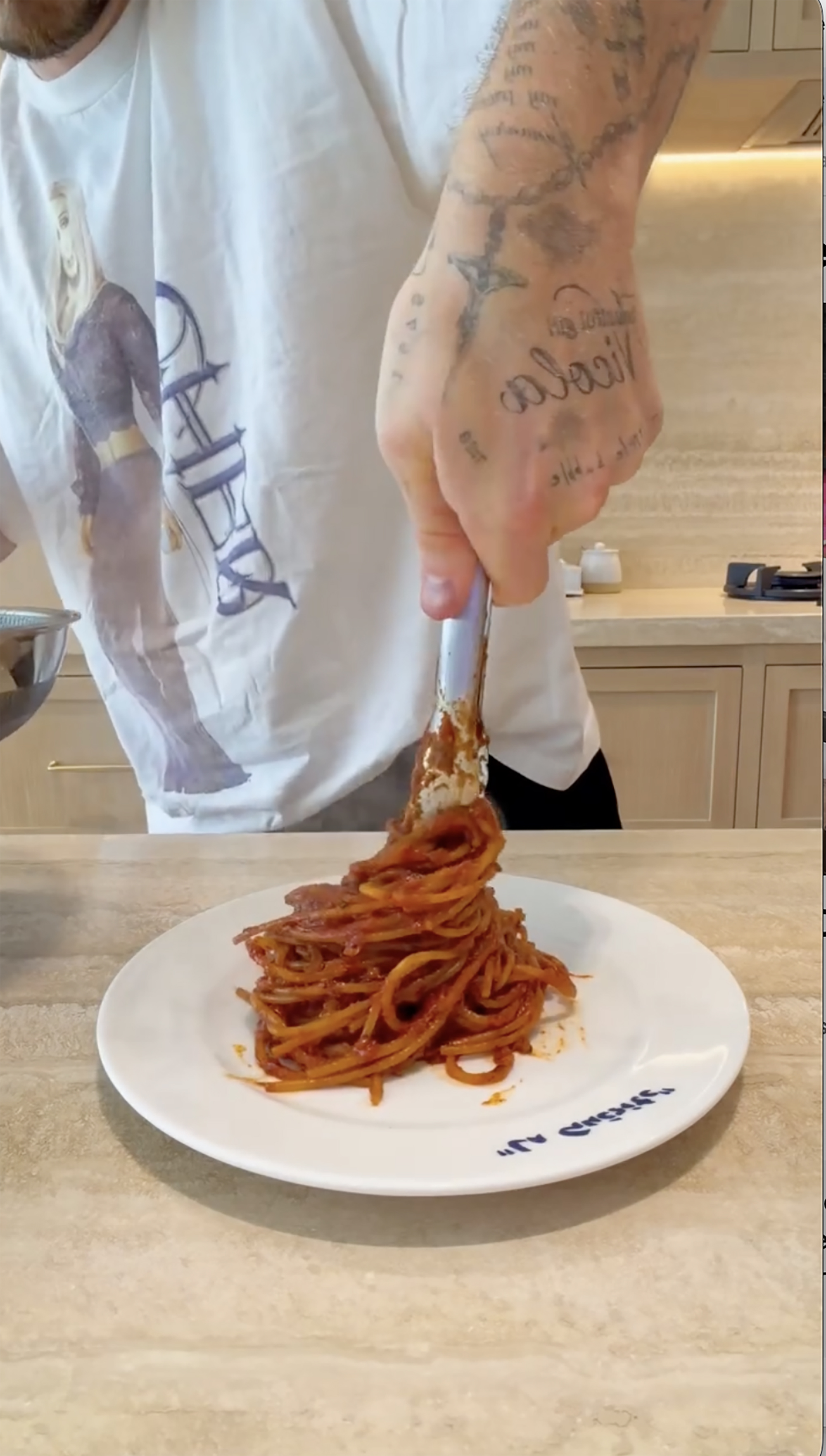 A person serving spaghetti with tomato sauce onto a white plate.