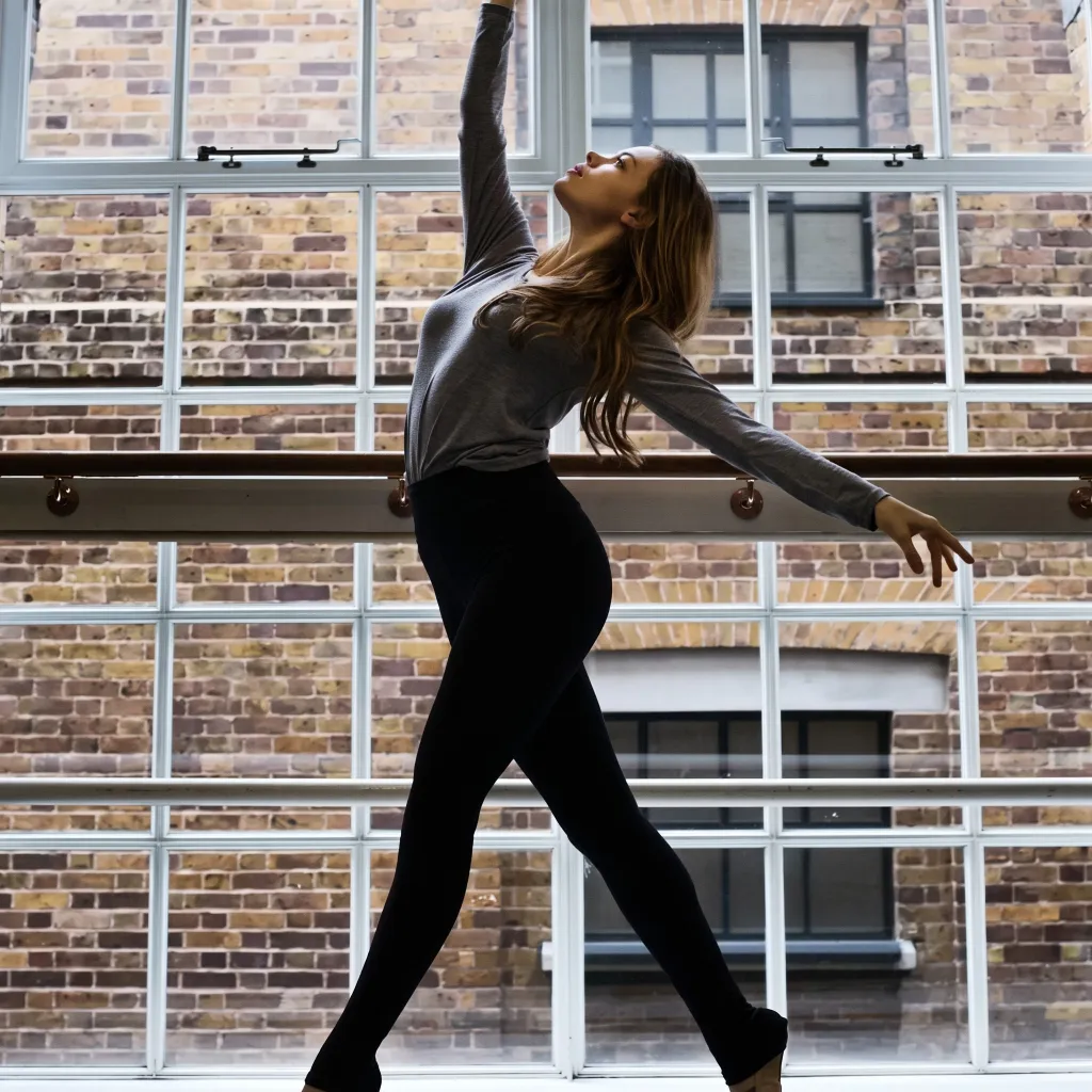 Eloise Skinner, a ballerina, in a studio with a high ceiling, looking upwards while holding her arm high.