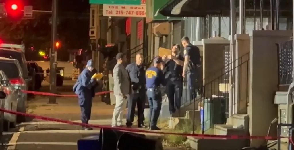 Police officers gather on the street behind crime scene tape after a shooting in West Philadelphia.