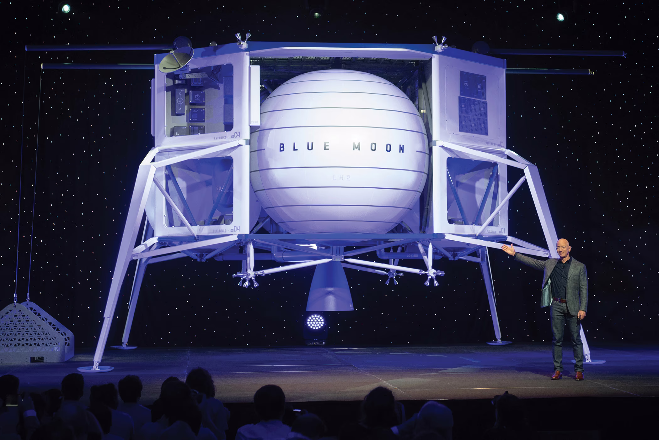 photo of Jeff Bezos on stage gesturing toward huge image of lunar lander