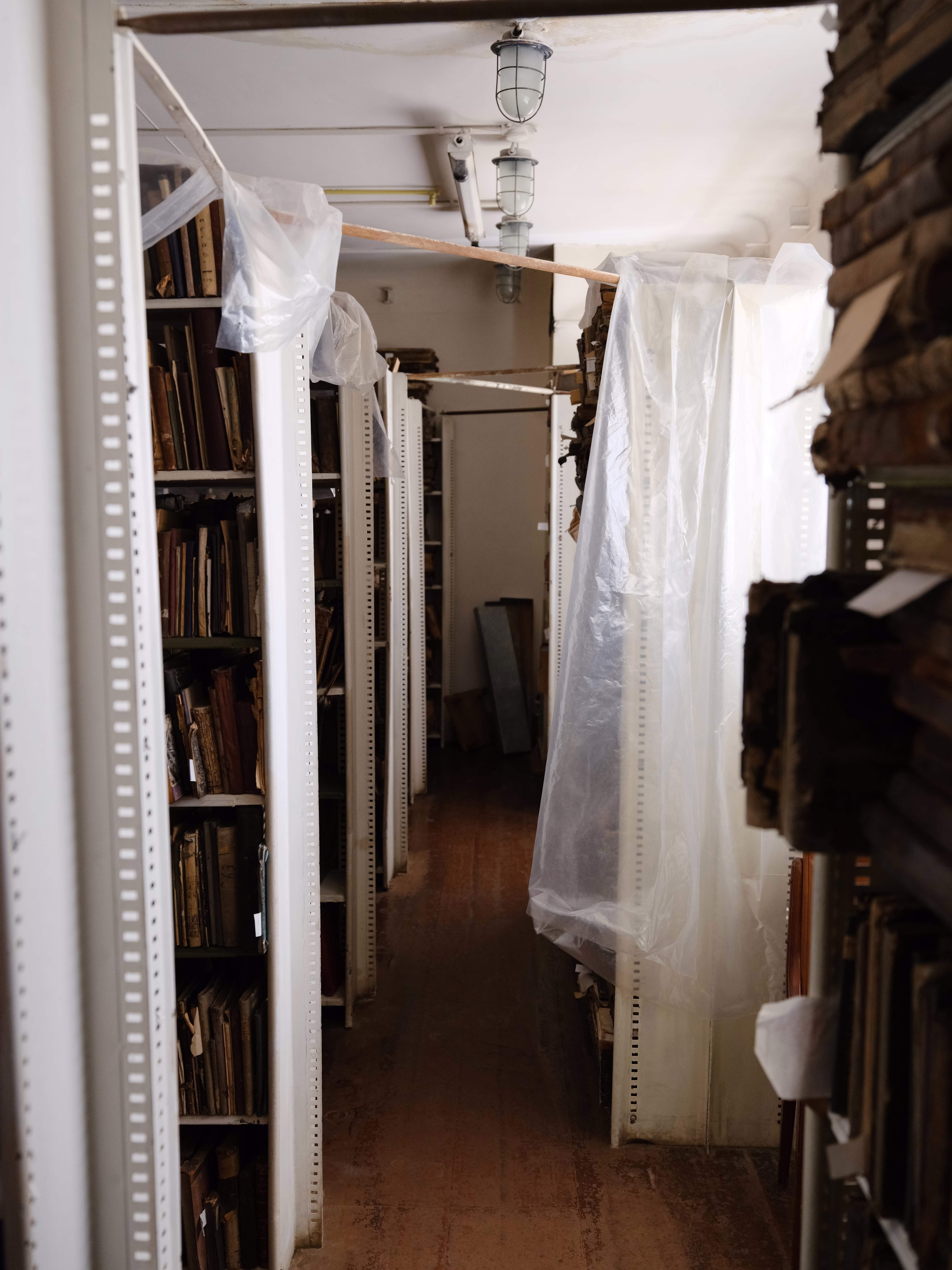 photo of room with wooden floor and shelves of books, with clear plastic sheets hanging over many of them