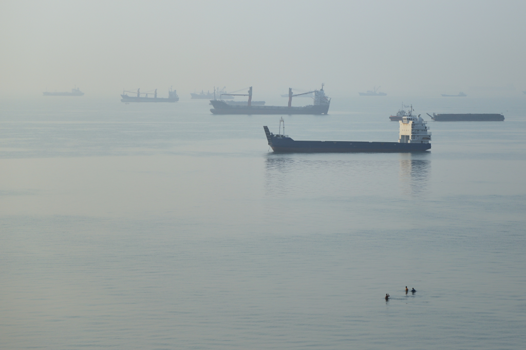People wade in the water as cargo ships are anchored in the Strait of Hormuz off Bandar Abbas, Iran.