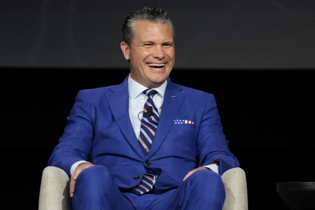 U.S. Defense Secretary Pete Hegseth seated in a blue suit at a panel discussion on autonomous warfare.