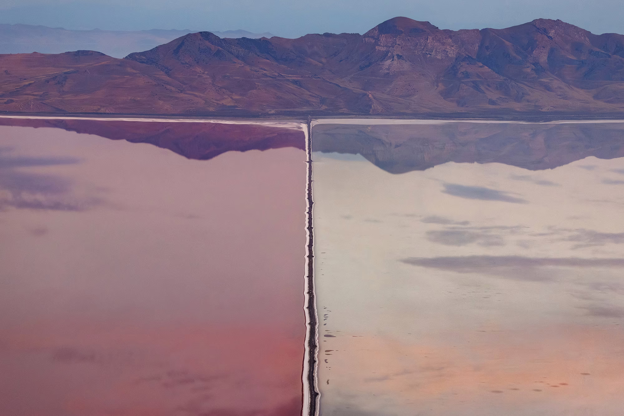 A view of a dividing dam in Utah’s Great Salt Lake, with two different bodies of water seen in varying hues of pink