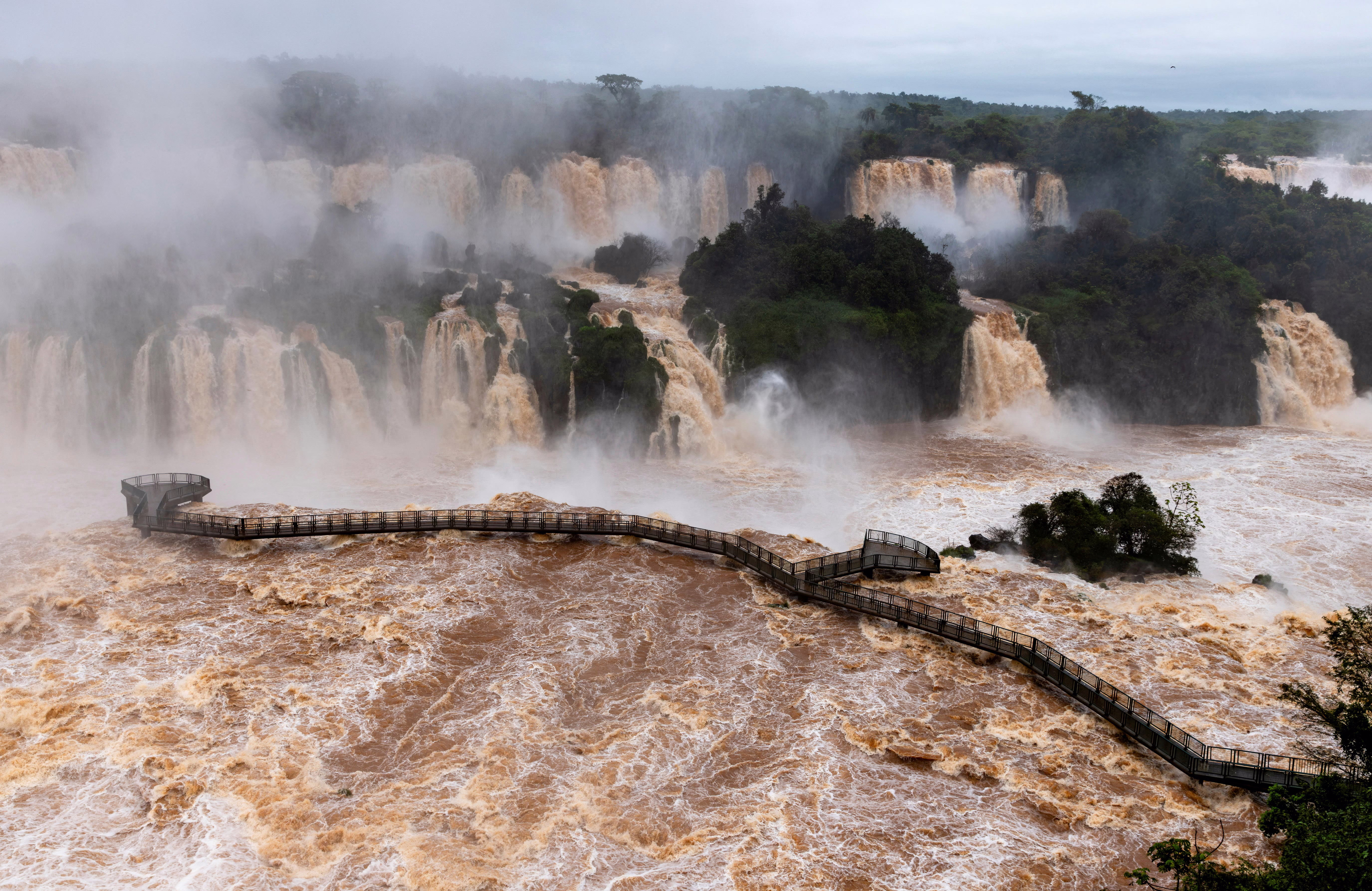 A closed walkway spans across part of a large and complex waterfall that is overflowing with high water.