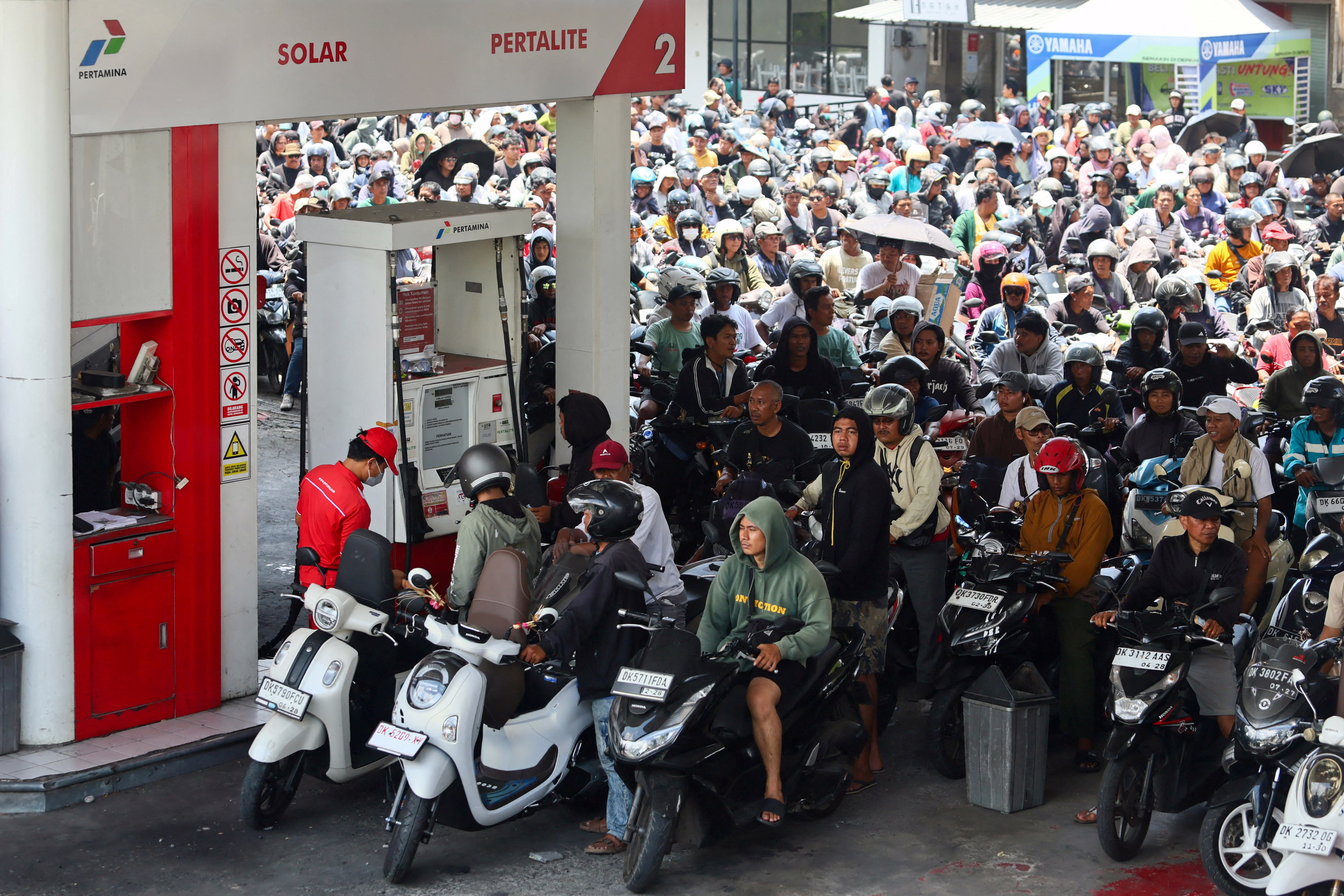 Many dozens of scooter and motorcycle riders jam into a queue at a gas station.