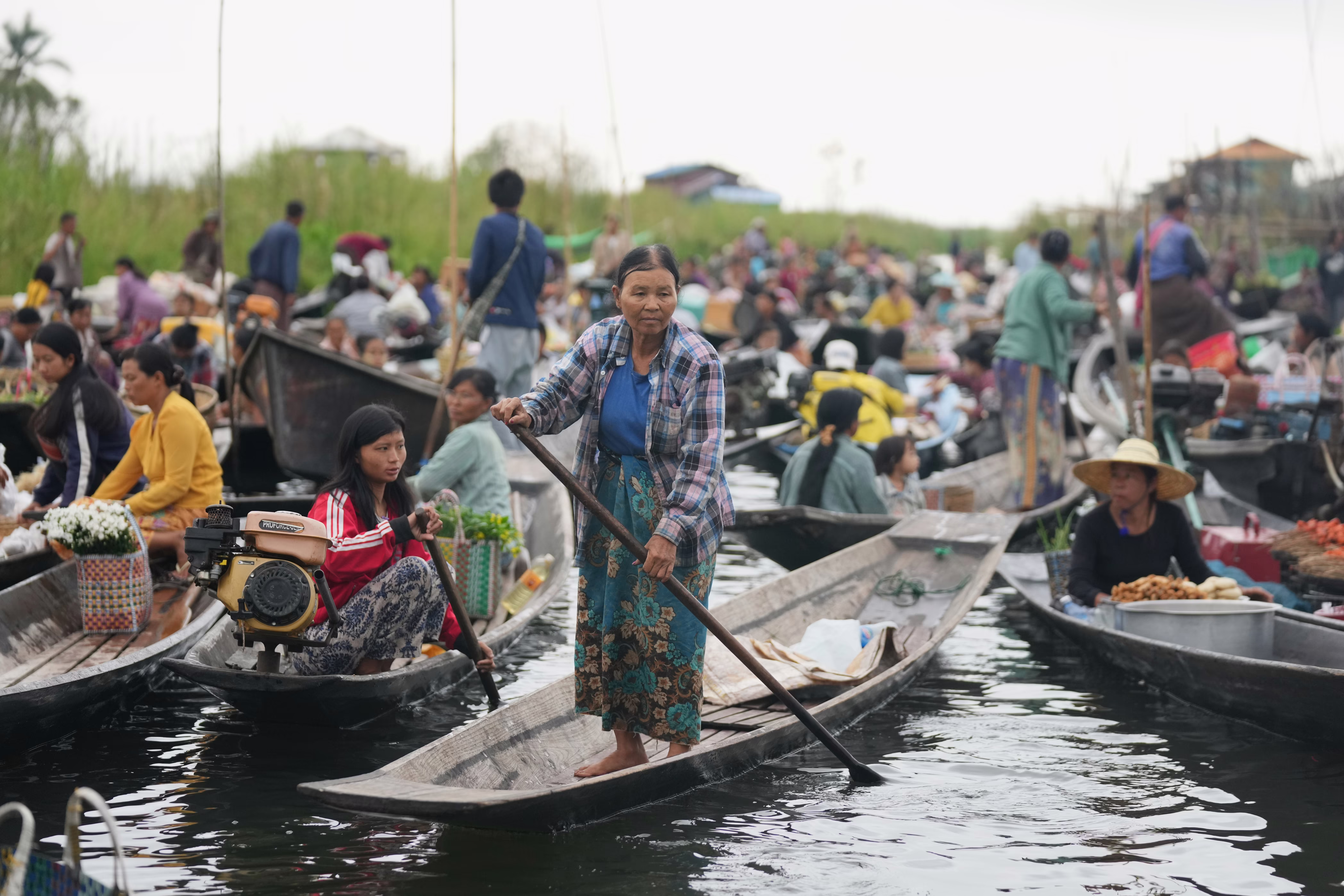 Many people sit and stand in dozens of small boats during a floating bazaar.