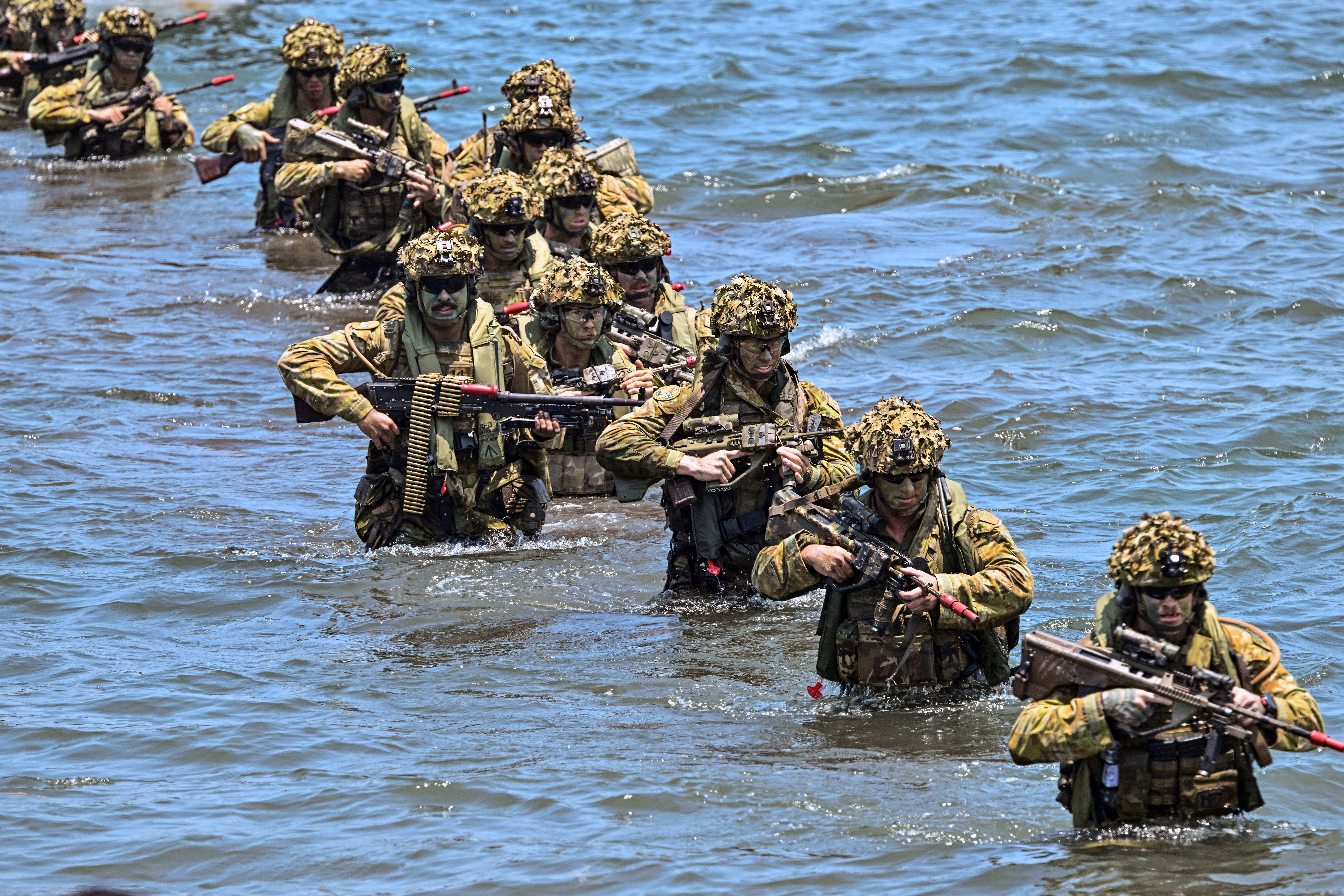 Soldiers carry long guns and heavy gear as they wade through waist-deep water.