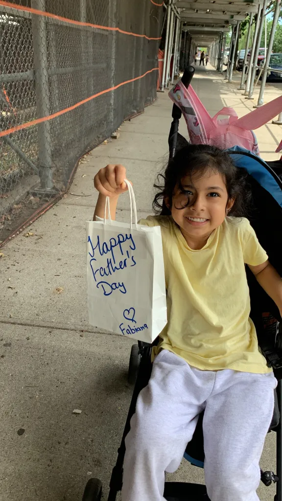 Fabiana Cabello smiling in a stroller and holding a gift bag with