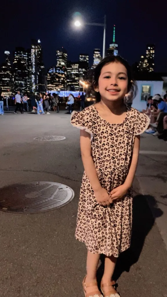 Fabiana Cabello smiling in a leopard-print dress with a city skyline in the background at night.