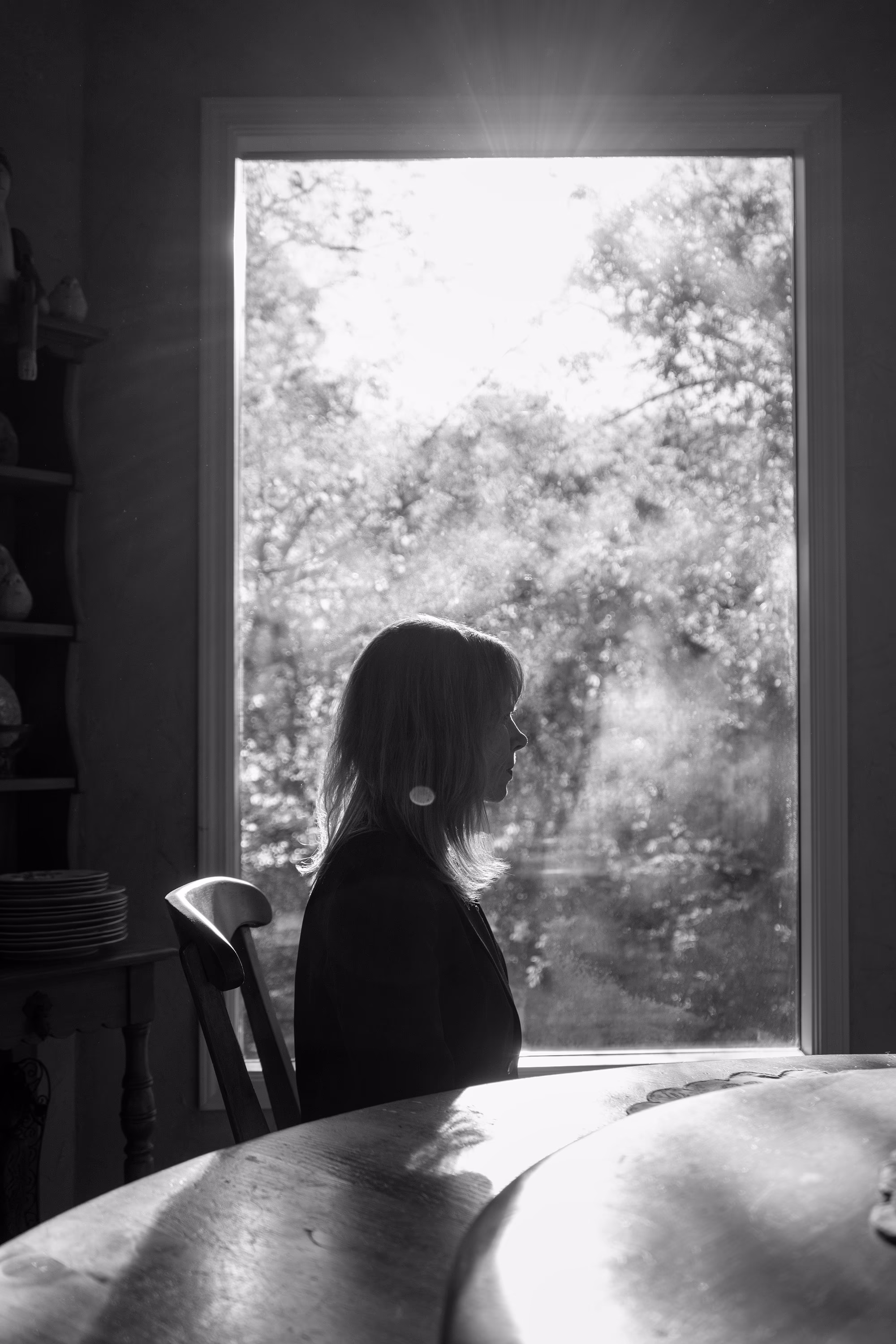 A black and white portrait of Cyndy sitting in front of a window