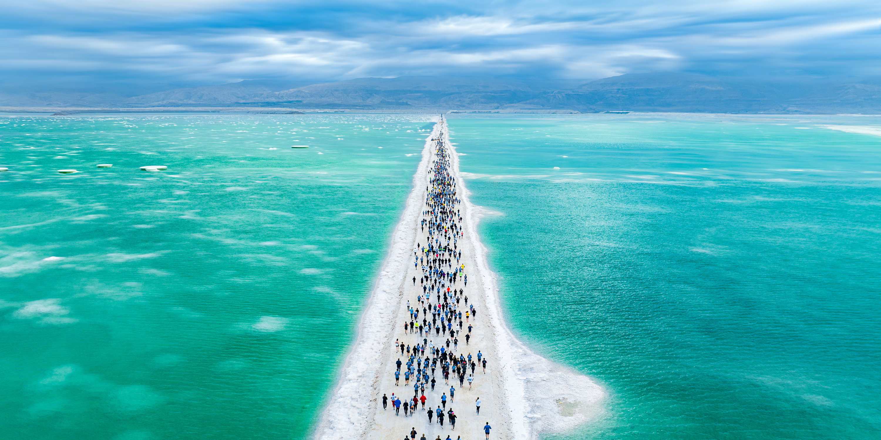An elevated view of runners racing along a raised road surrounded by water on either side