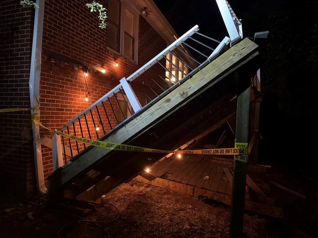 A collapsed wooden deck sits behind police tape at a Williamsburg, Virginia, home after a homecoming party incident injured at least 28 people