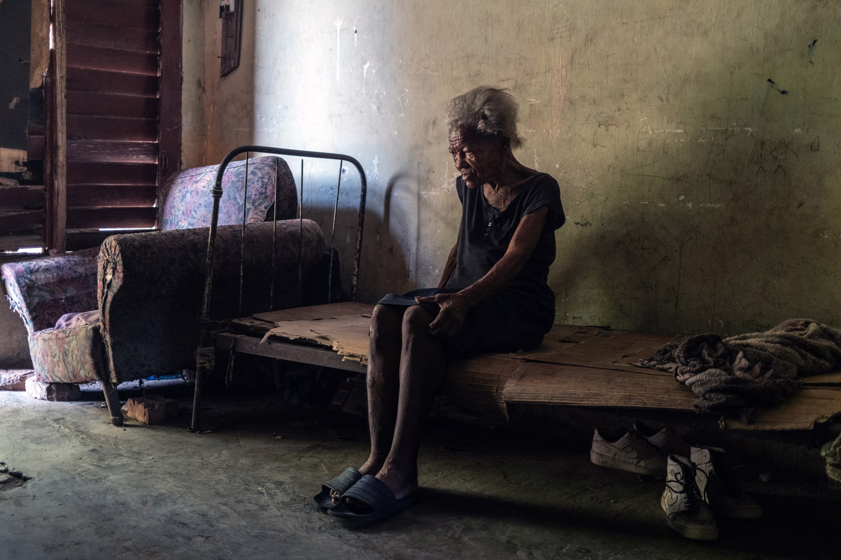 an old woman sits on card board on a metal bed frame