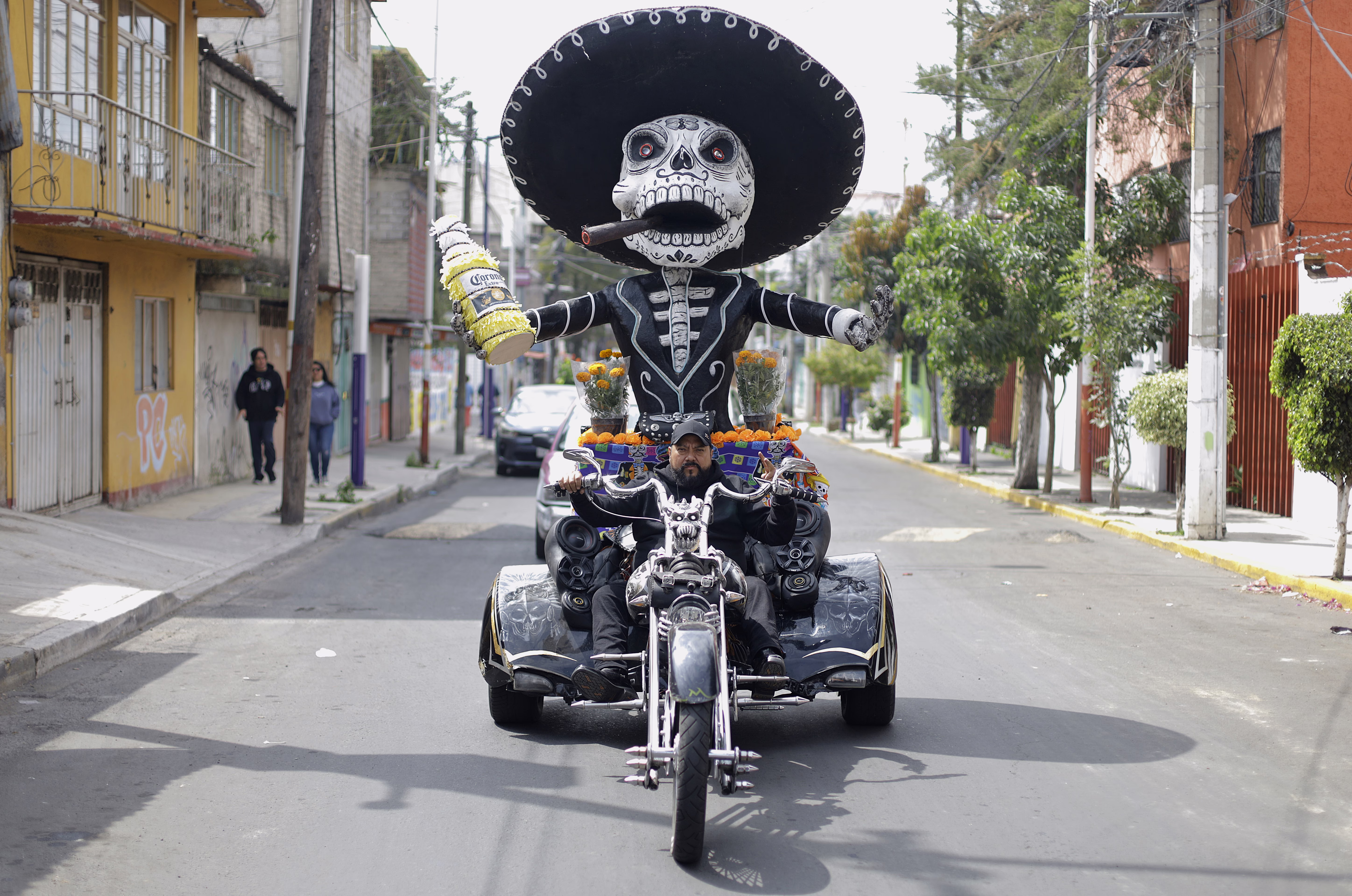 A person drives a three wheeled motorcycle with a traditionally-decorated skeleton statue riding on the back.
