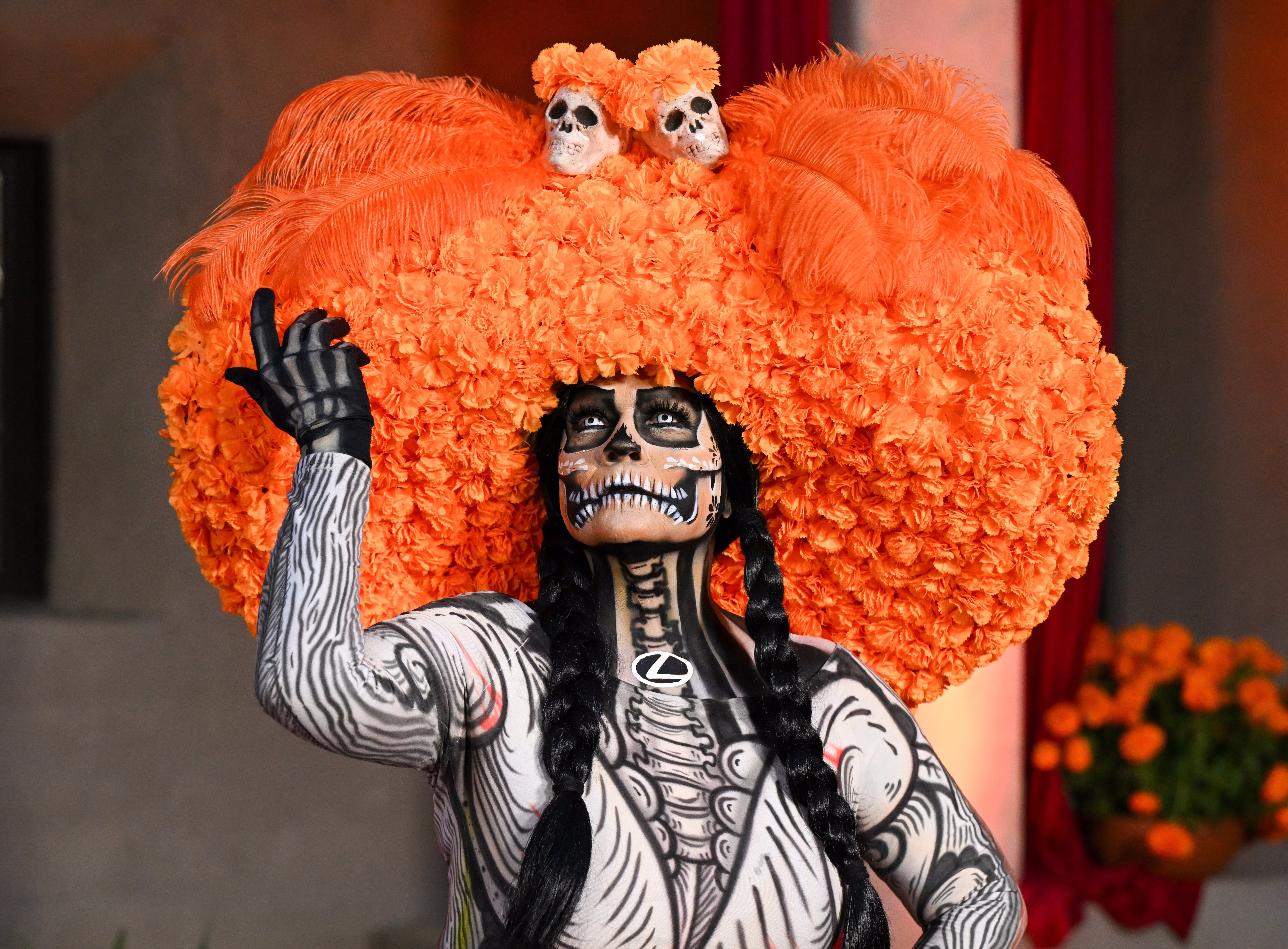 A person poses, wearing skeletal makeup, costume, and a large floral headdress.