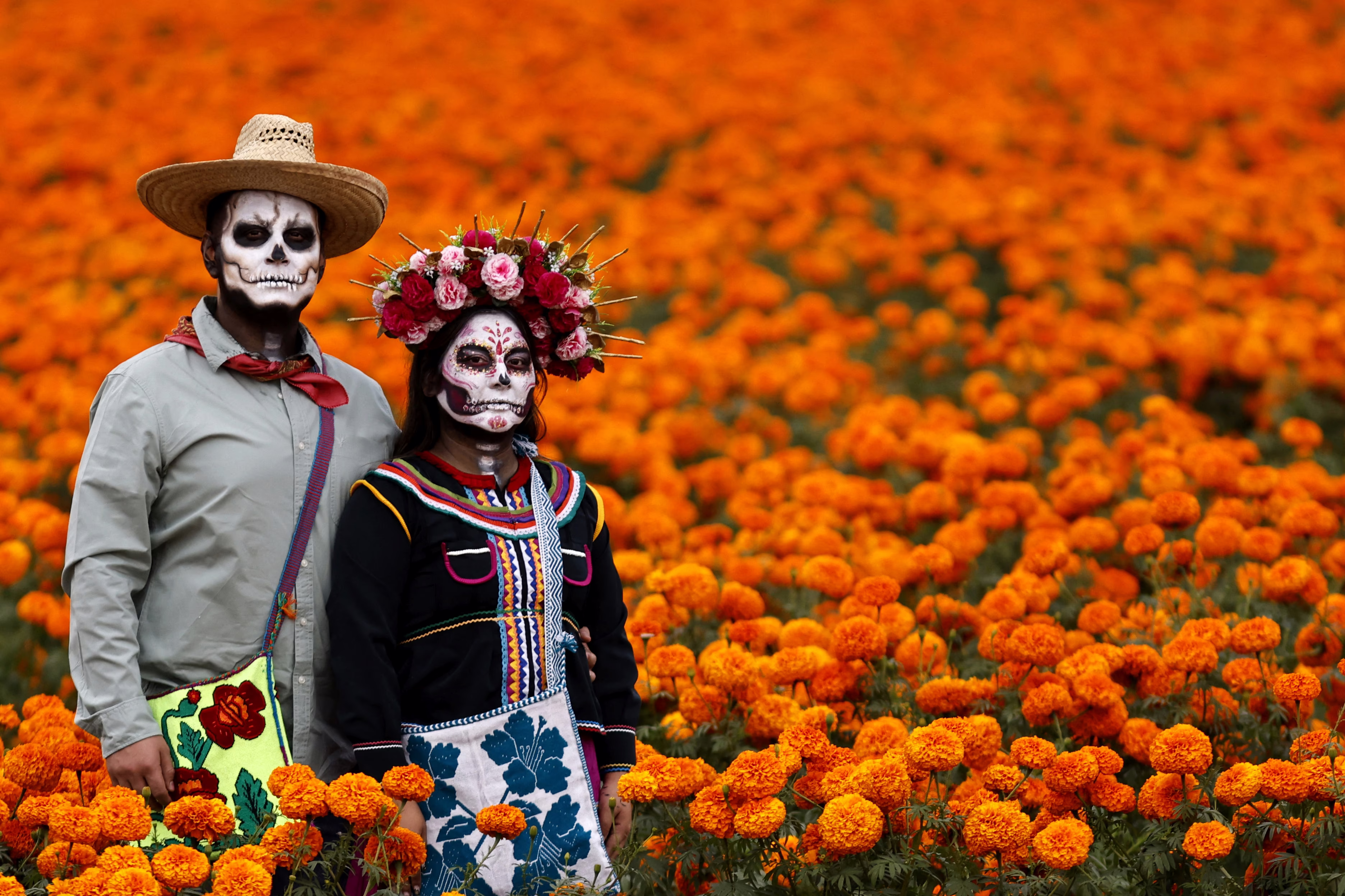 A couple wearing skeletal makeup poses in a field of orange flowers.