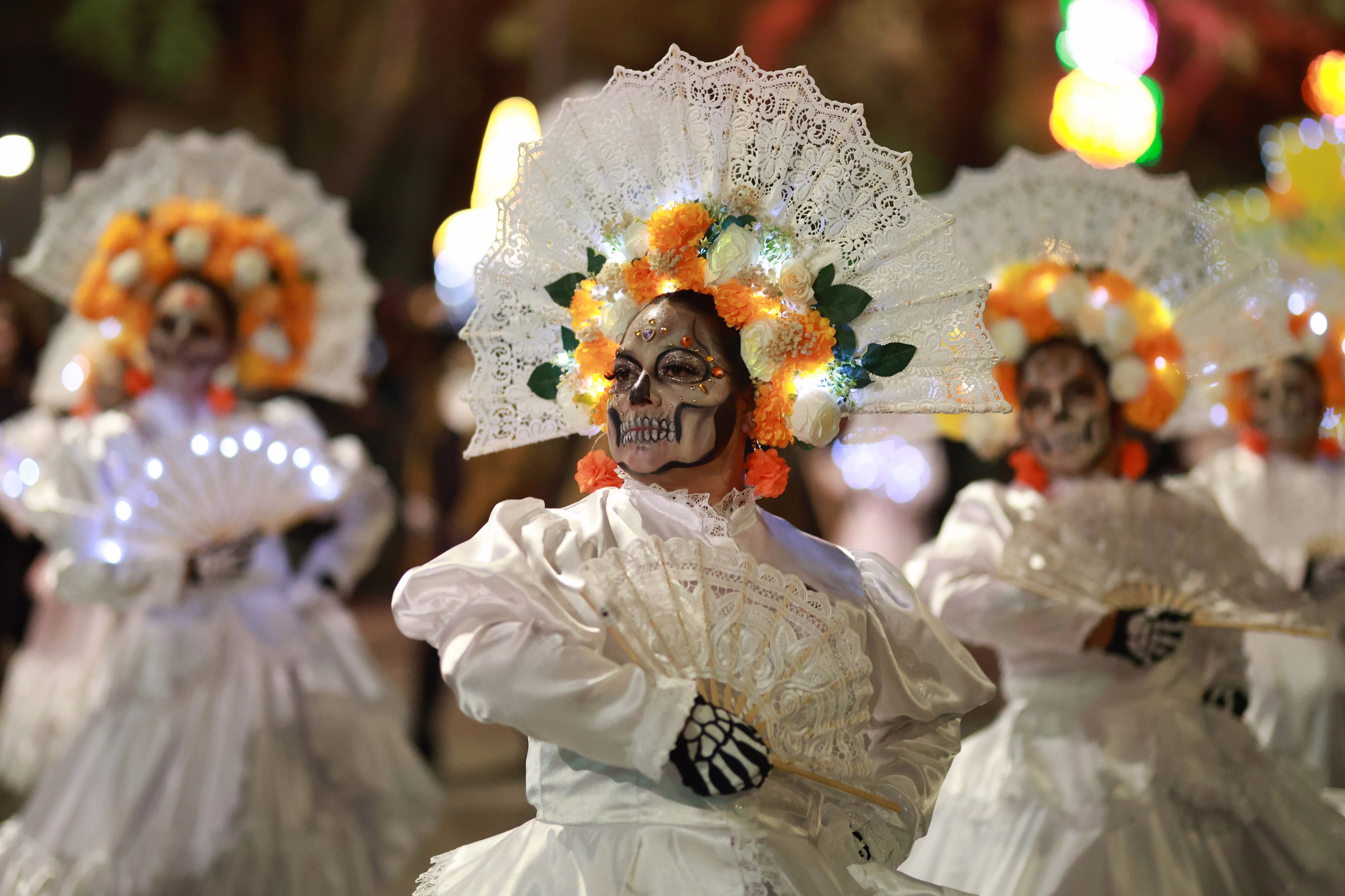 People in costumes and skeletal makeup dance in a parade.