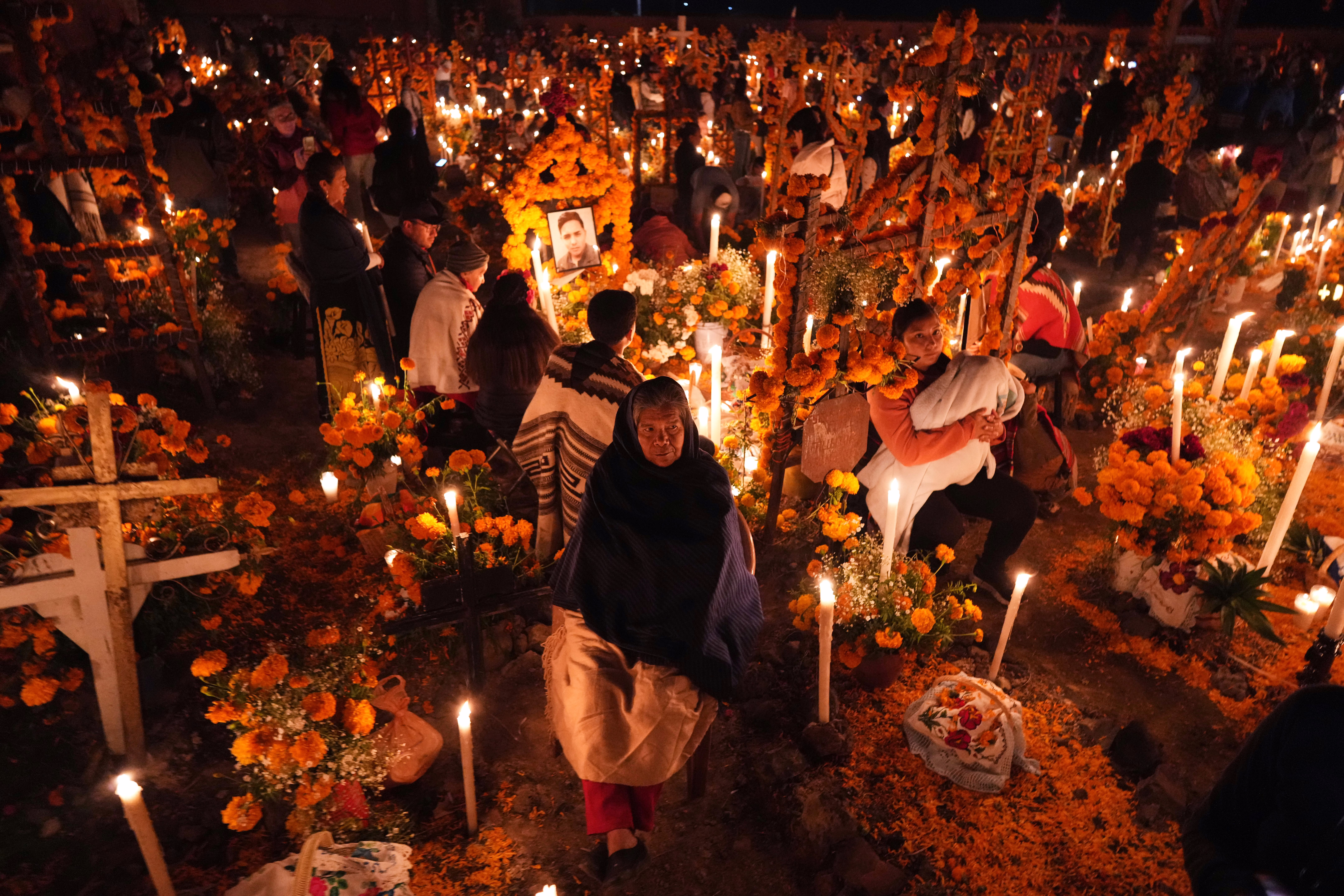 Many people gather in a cemetery, among hundreds of lit candles, on the Day of the Dead.