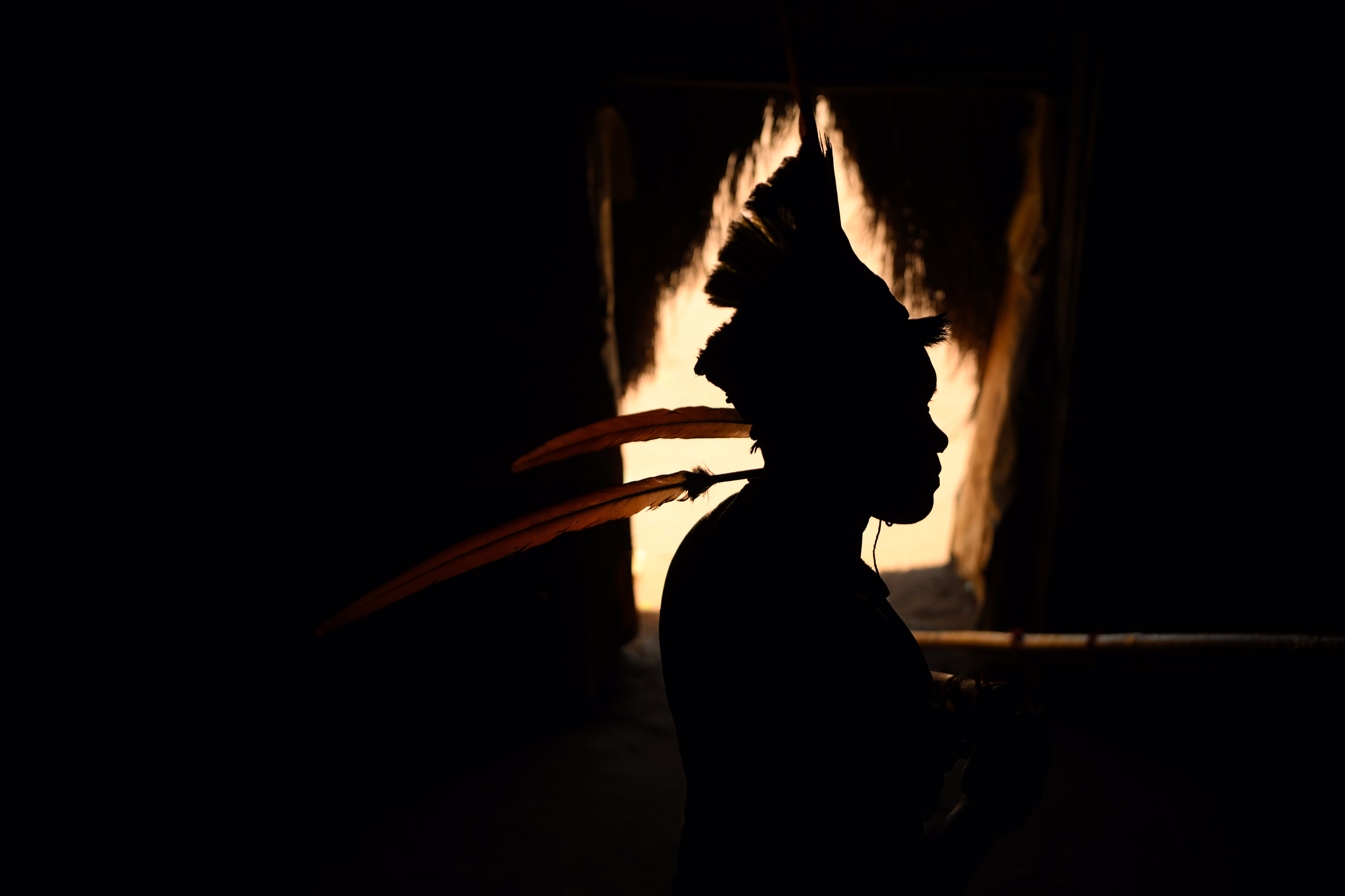 A member of a Brazilian indigenous group, wearing a traditional headdress, seen in silhouette