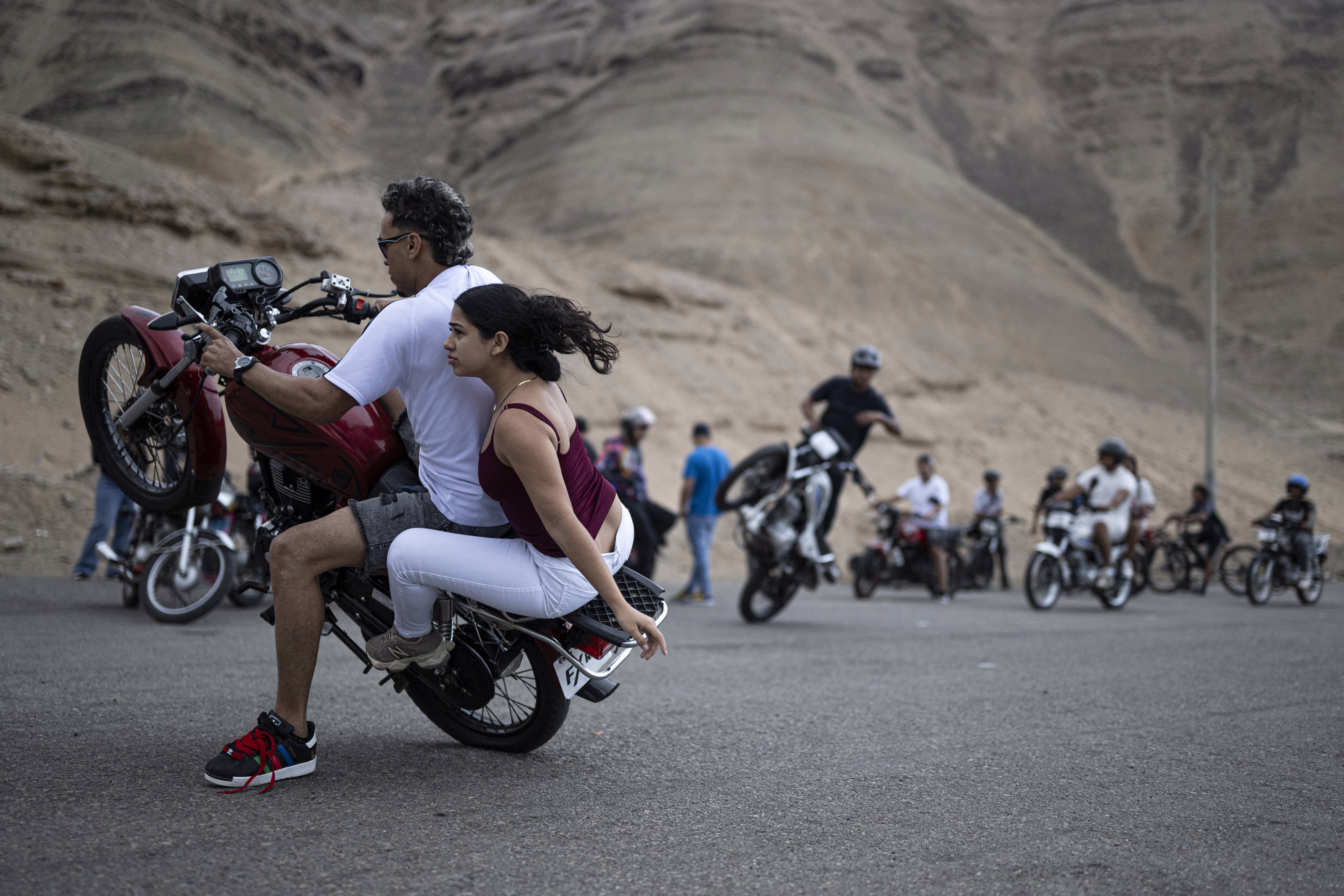 People perform tricks on motorcycles as others watch.