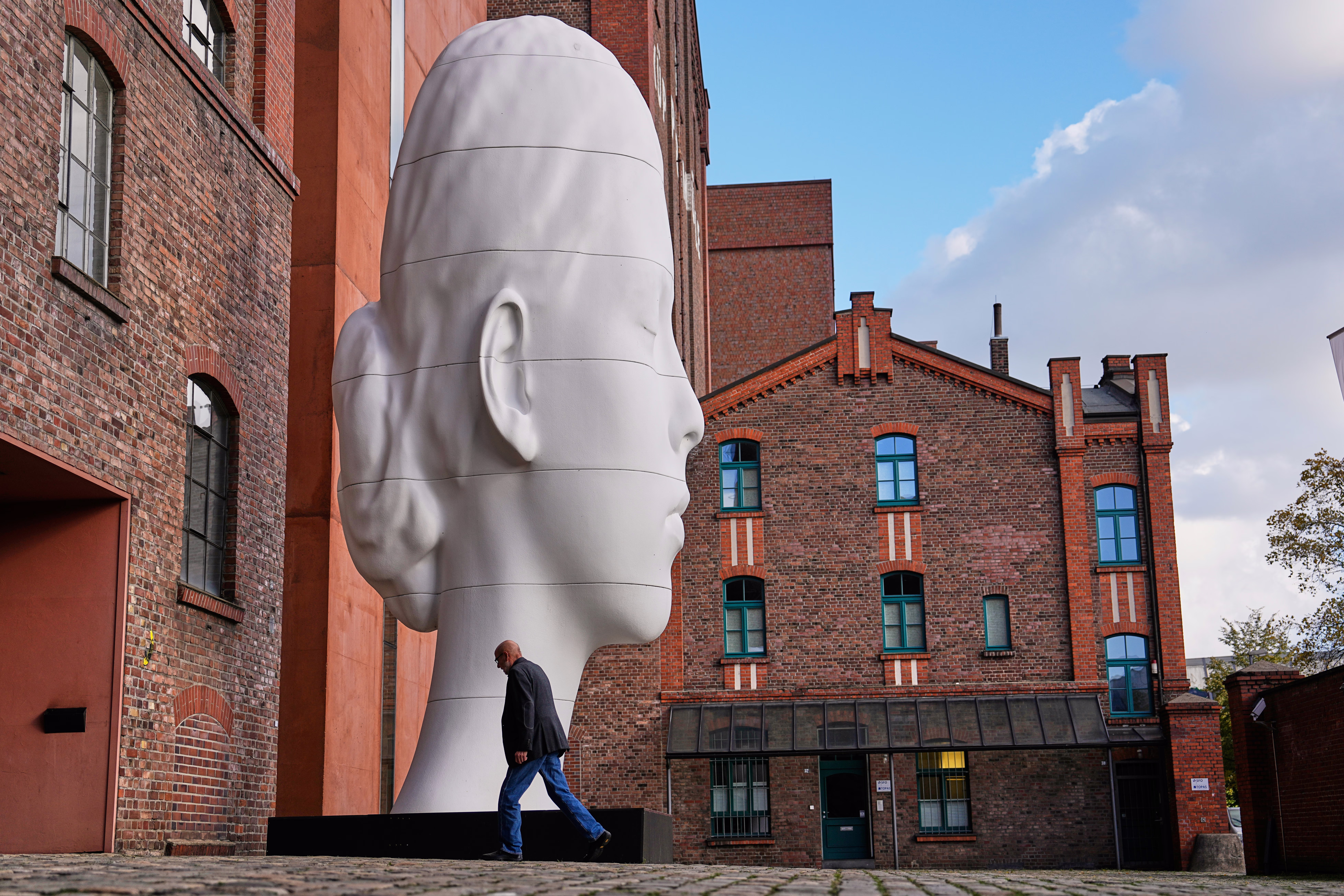 A person enters a museum, walking past a tall, elongated sculpture of a person's head. 