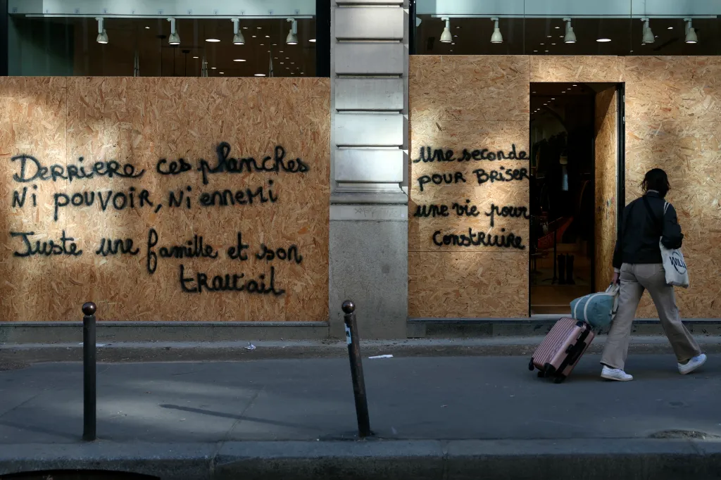 A pedestrian walks past a shop in Paris with storefront windows boarded up and spray-painted with French messages ahead of nationwide protests.