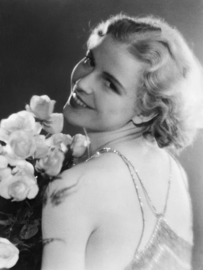 Portrait of Inga Arvad, Miss Denmark 1931, holding a bouquet of roses and smiling at the camera.