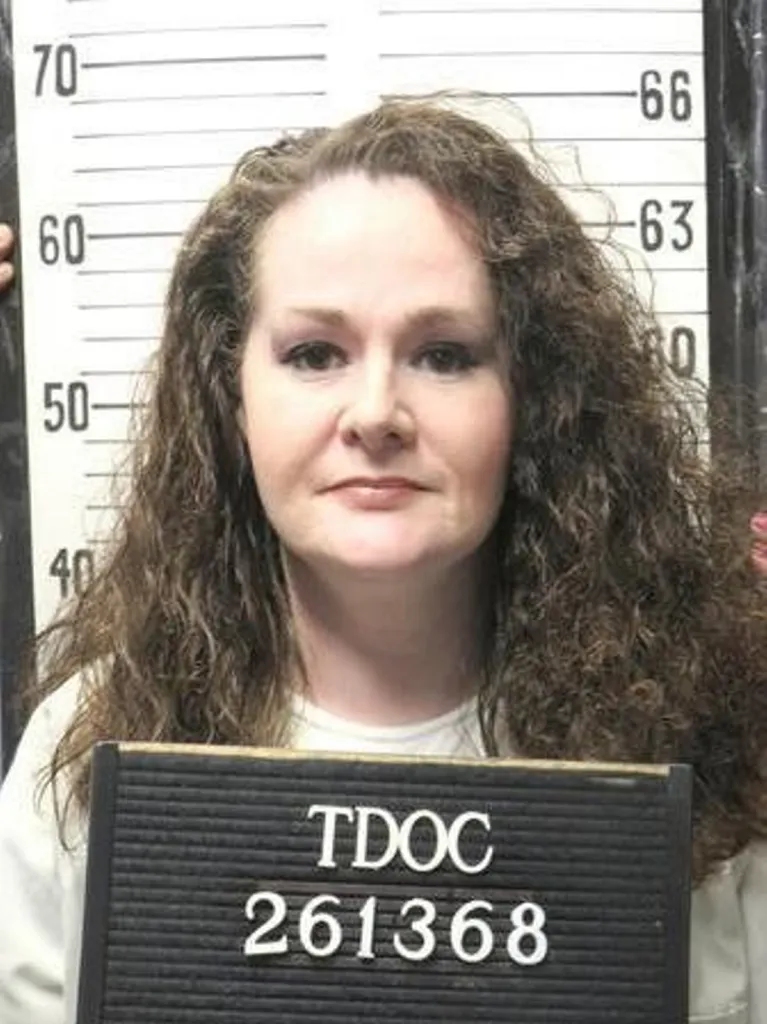 Booking photo of Christa Pike in front of a height chart holding a sign with her inmate number.