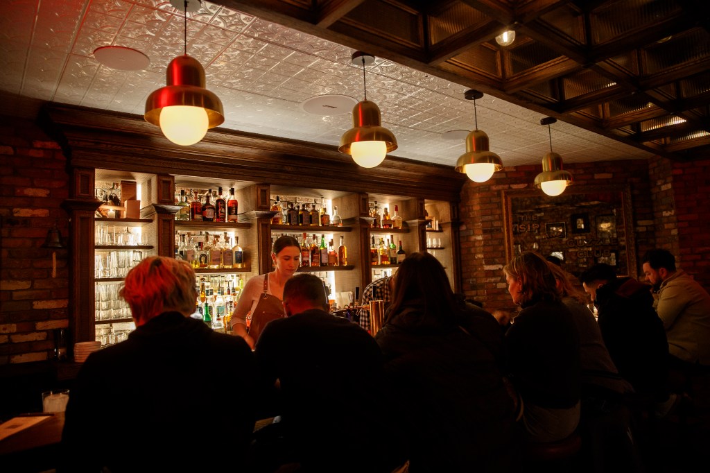 Patrons sit at the bar while a bartender stands behind the counter at Guzzle.