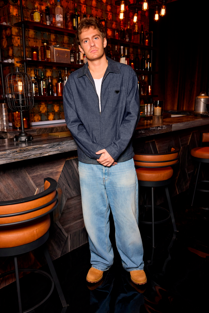 Charlie Zakkour stands in a bar with shelves of liquor bottles in the background.