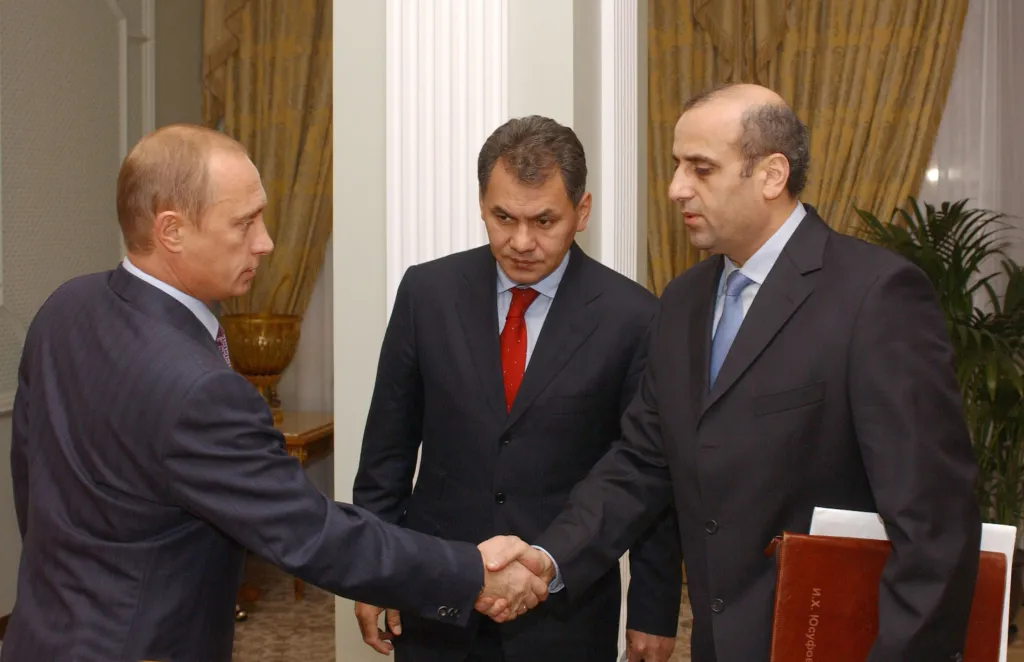 Russian President Vladimir Putin shakes hands with Energy Minister Igor Yusufov while Emergencies Minister Sergei Shoigu looks on.