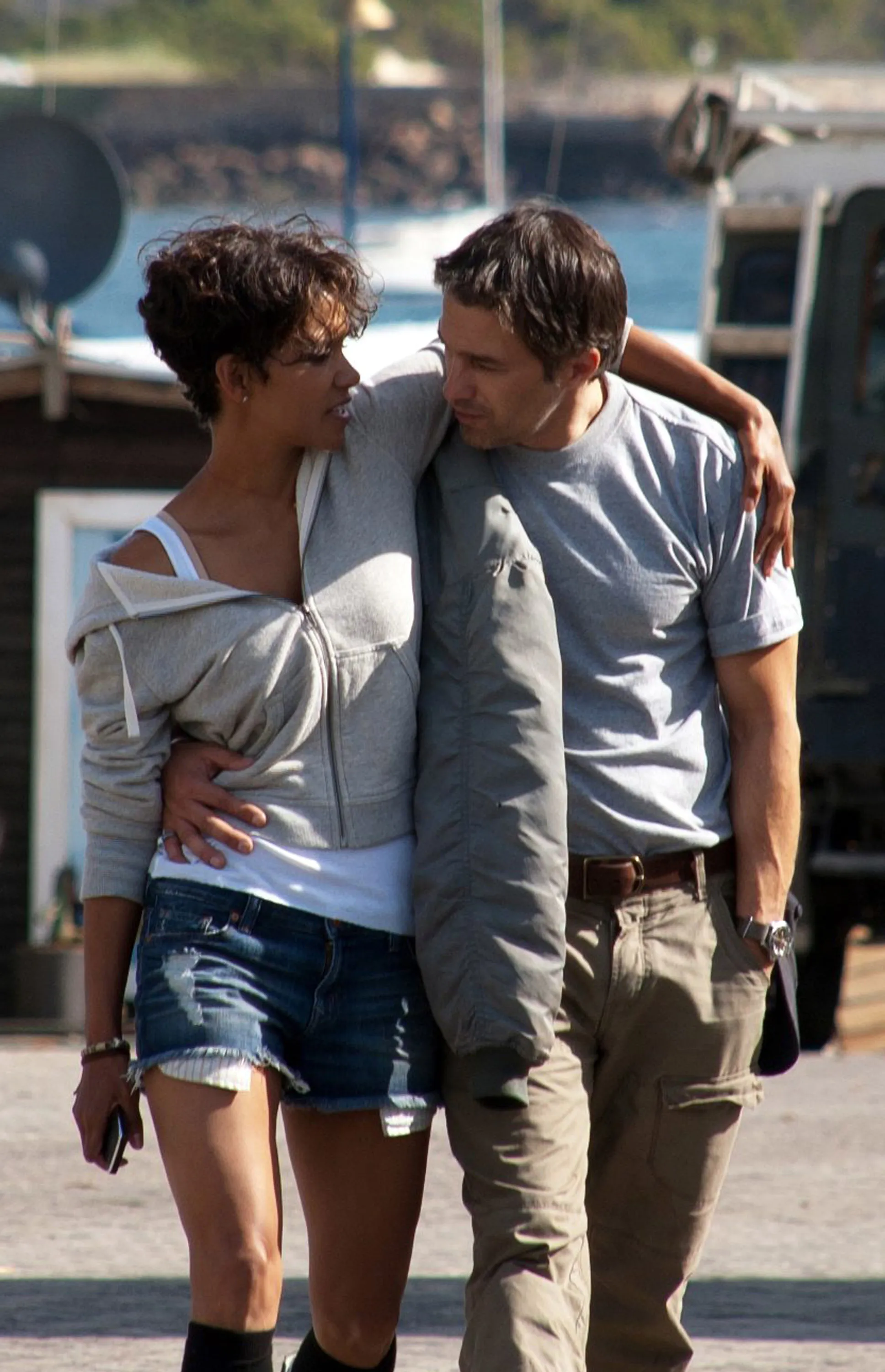Actors Halle Berry and Olivier Martinez walk closely together with their arms around each other near a harbor during the filming of Dark Tide.