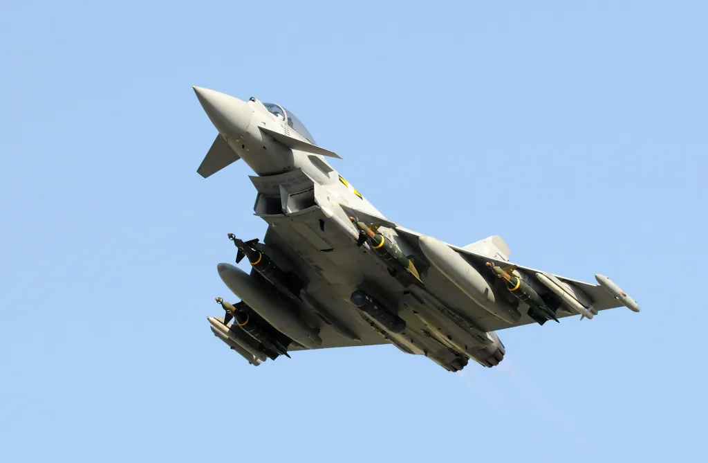A Royal Air Force Typhoon fighter jet in flight, carrying missiles and fuel tanks.