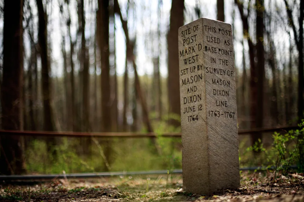 A stone post marking the base point for the Mason-Dixon survey, set in a wooded area in Newark, Delaware.
