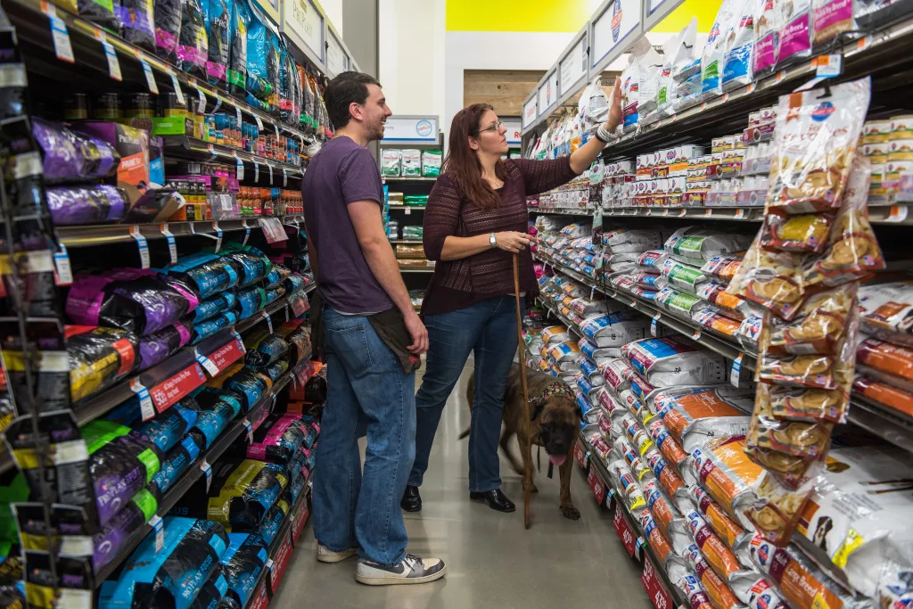An employee assists a customer with dog food at a Petco store.