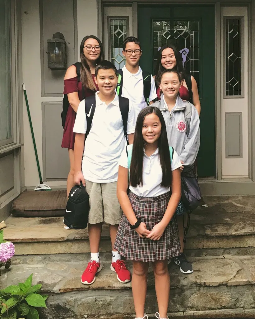 Six young people stand outside a house with backpacks on, ready for school.