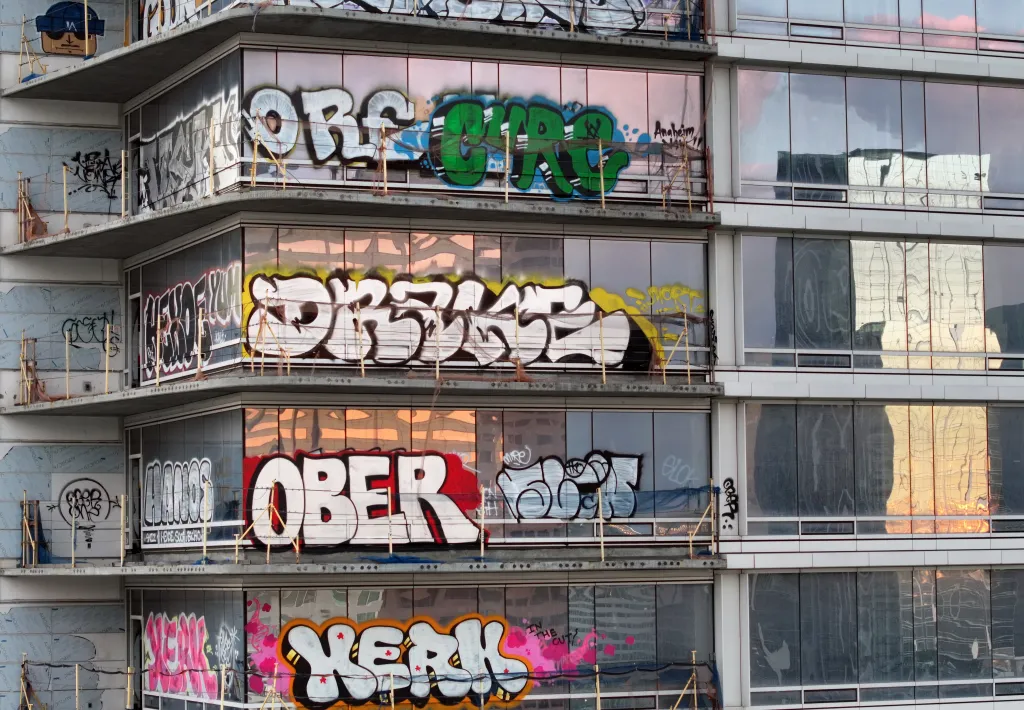 Graffiti covers the glass exterior of a multi-story unfinished high-rise building.