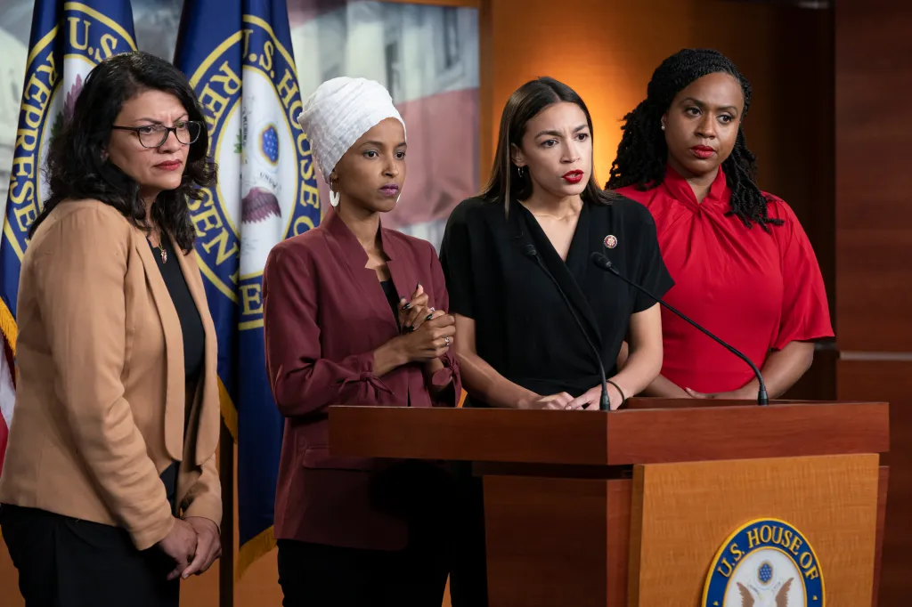 Reps. Rashida Tlaib, Ilhan Omar, Alexandria Ocasio-Cortez, and Ayanna Pressley standing at a podium for a news conference.