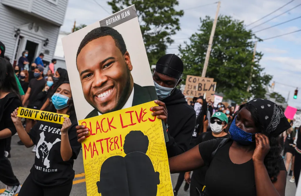 A demonstrator carries a large sign featuring Botham Jean and the words 