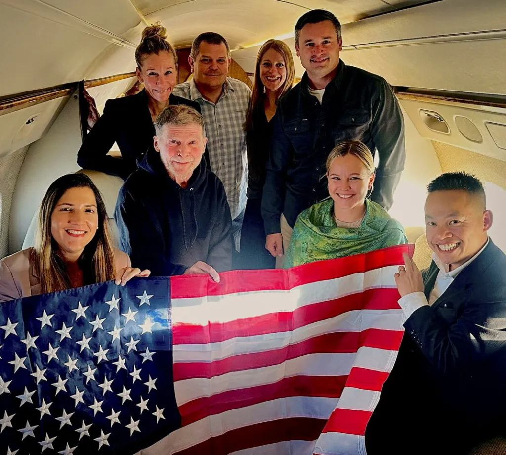 Stephen Hubbard, the 74-year-old American citizen held in Russian custody since 2022, poses with family members and US officials aboard a flight back to the US after his release from prison on Oct. 21, 2026.