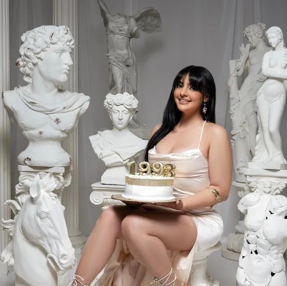 Officer Maria Delacruz holding a birthday cake amidst classical statues.